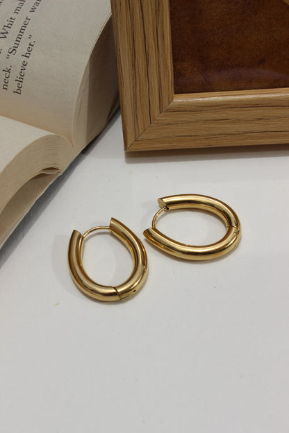 Aurume Earrings on a white surface with a wooden frame and book corner in the background