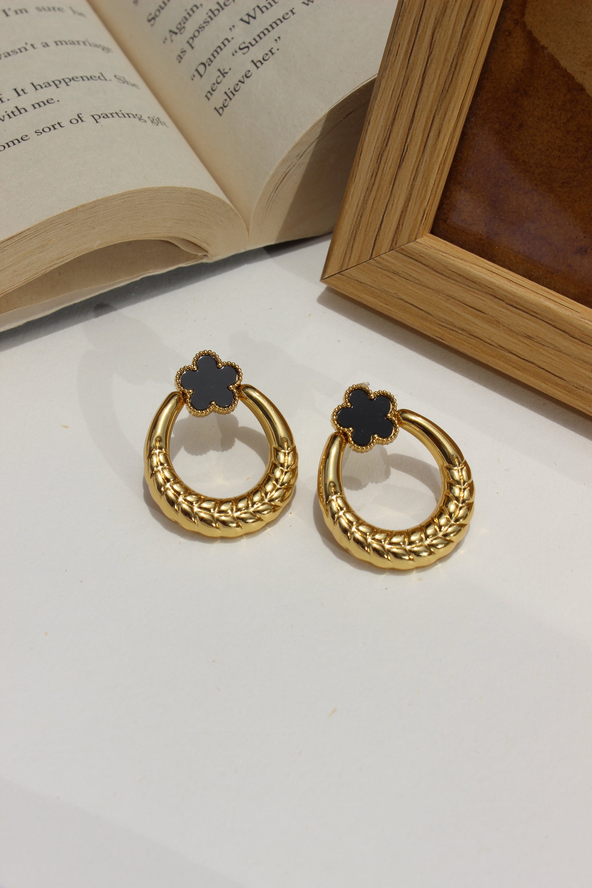 Orbella Earrings on a white surface next to an open book and wooden frame