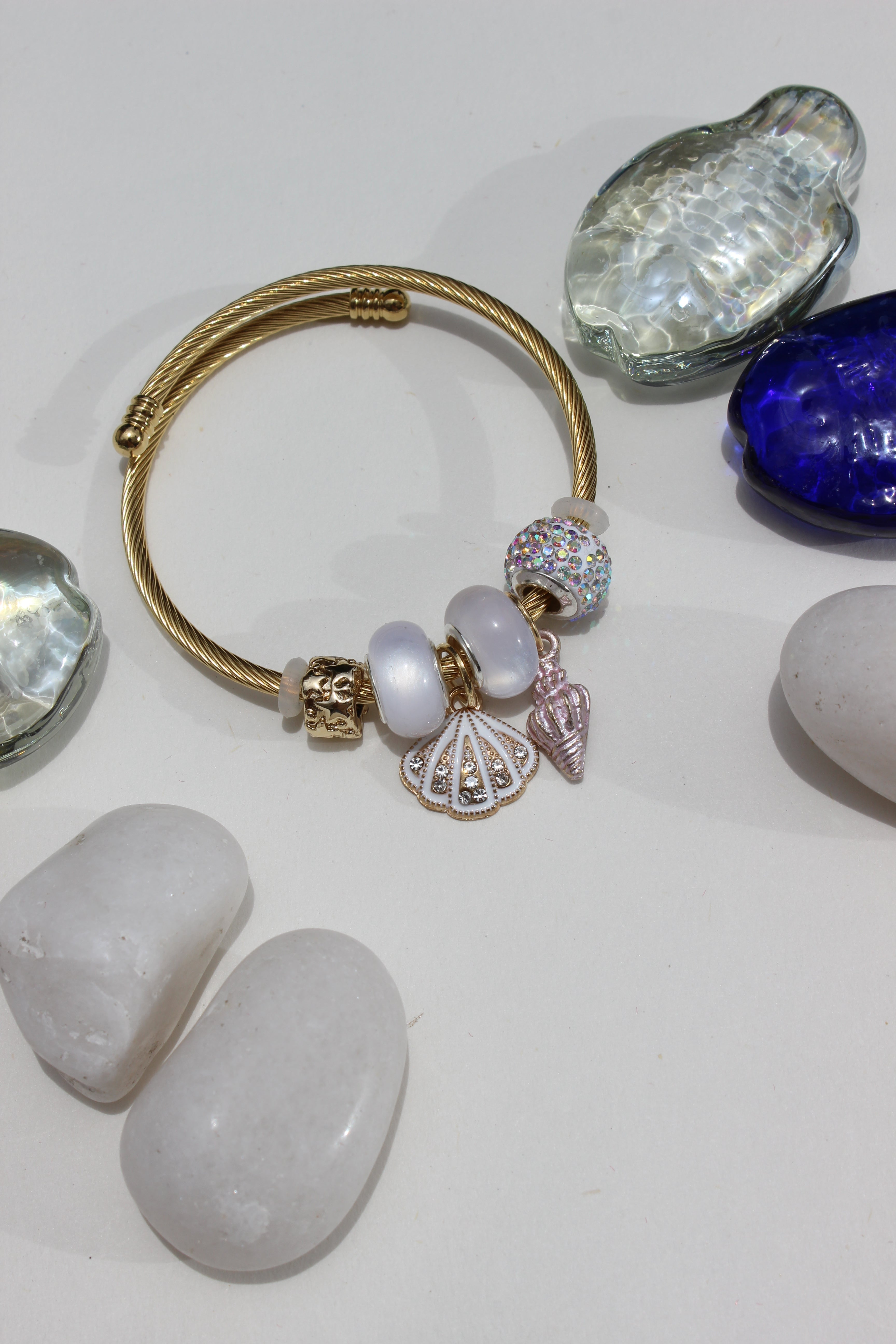 Alba Muse Charms Bracelet with charms on a white surface with seashells