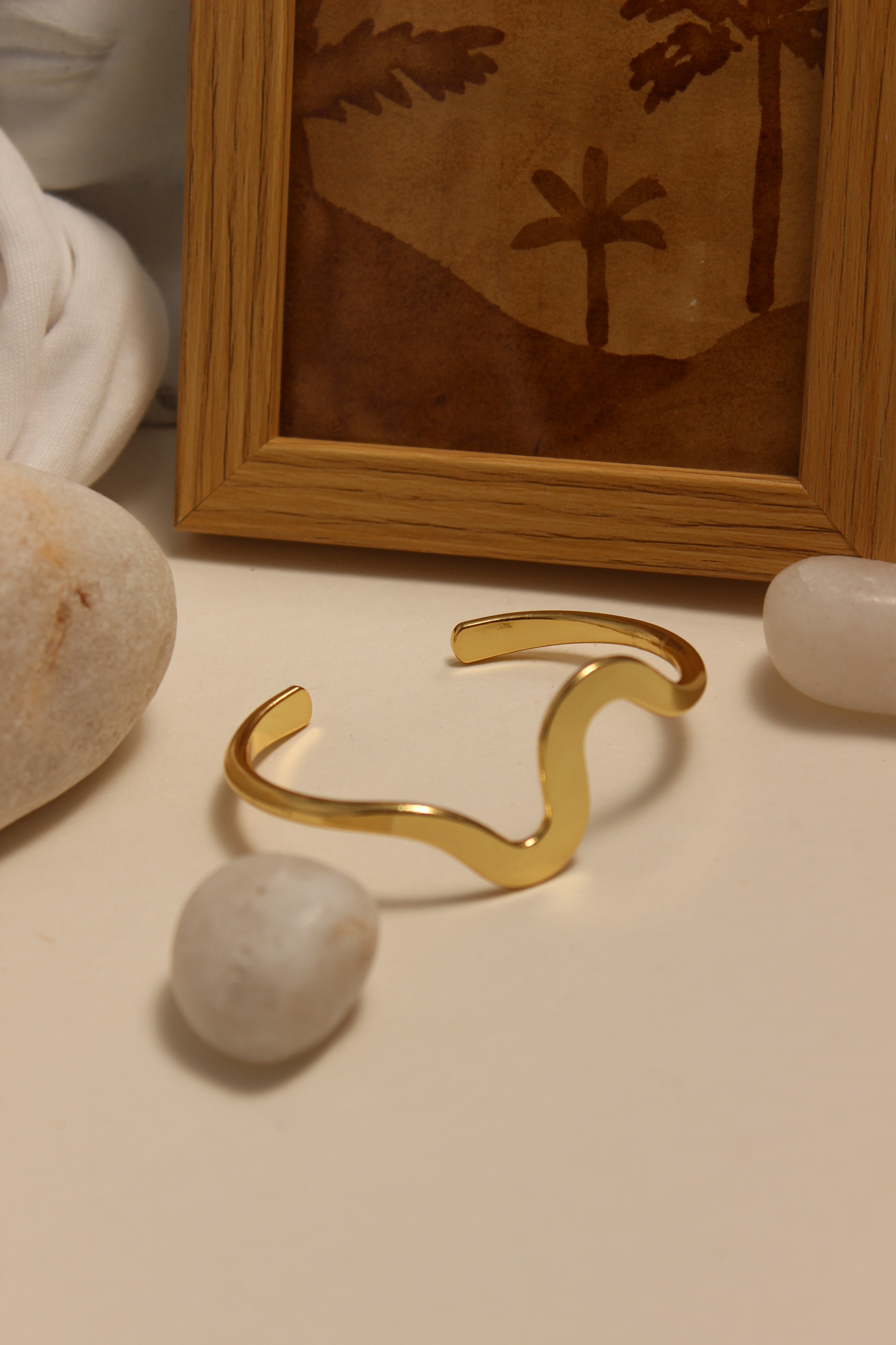 Magic Wave Cuff Bracelet on a beige wall next to a framed picture and stones