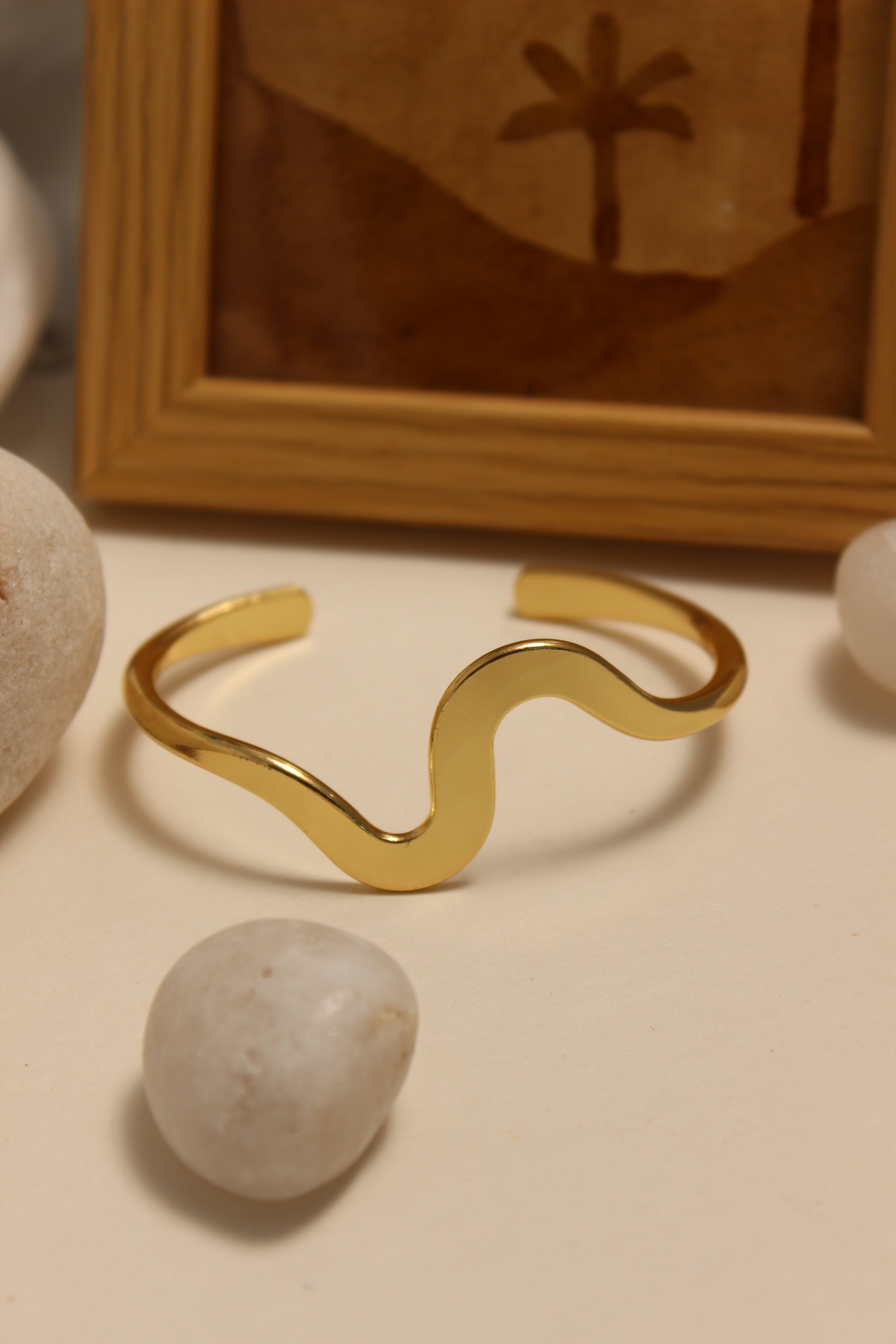 Magic Wave Cuff Bracelet on a beige wall with a framed picture and stones in the background