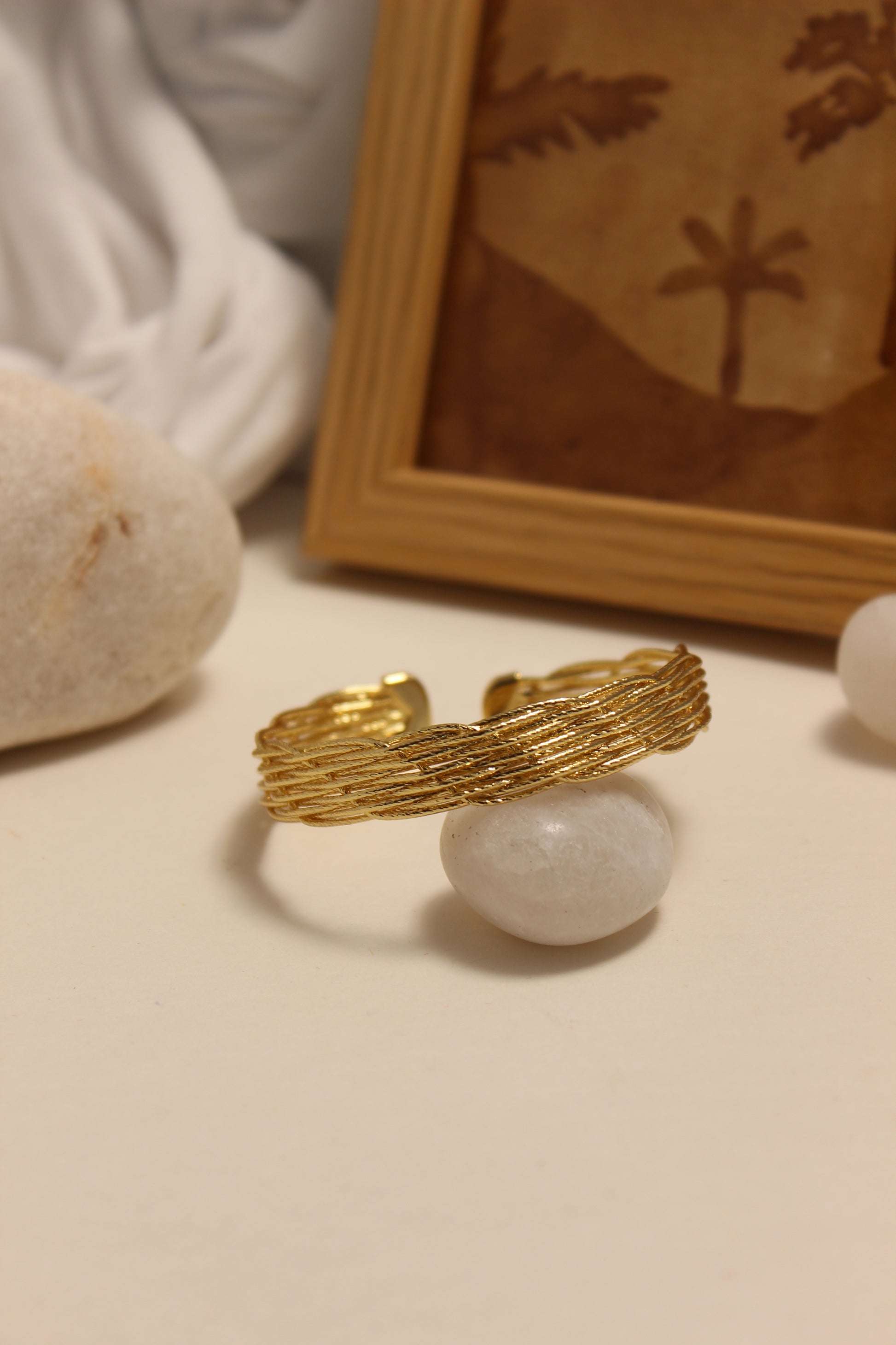Woven Gold Cuff Bracelet on a textured surface with a blurred background