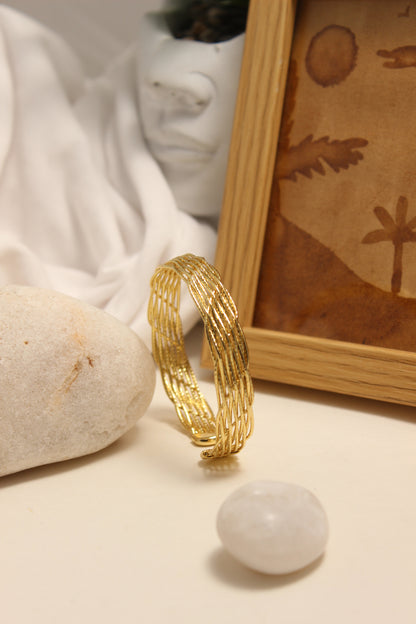 Woven Gold Cuff Bracelet on a textured surface with a blurred background