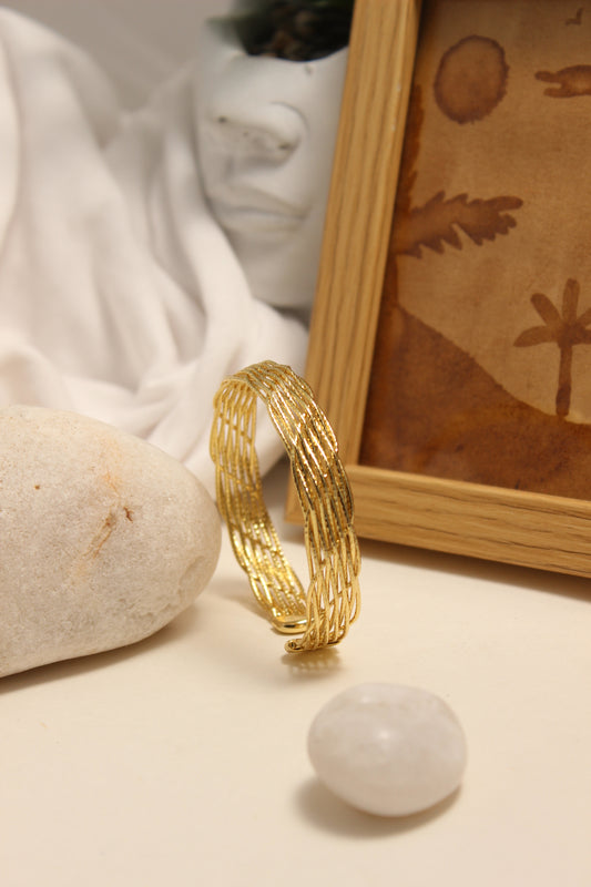 Woven Gold Cuff Bracelet on a textured surface with a blurred background