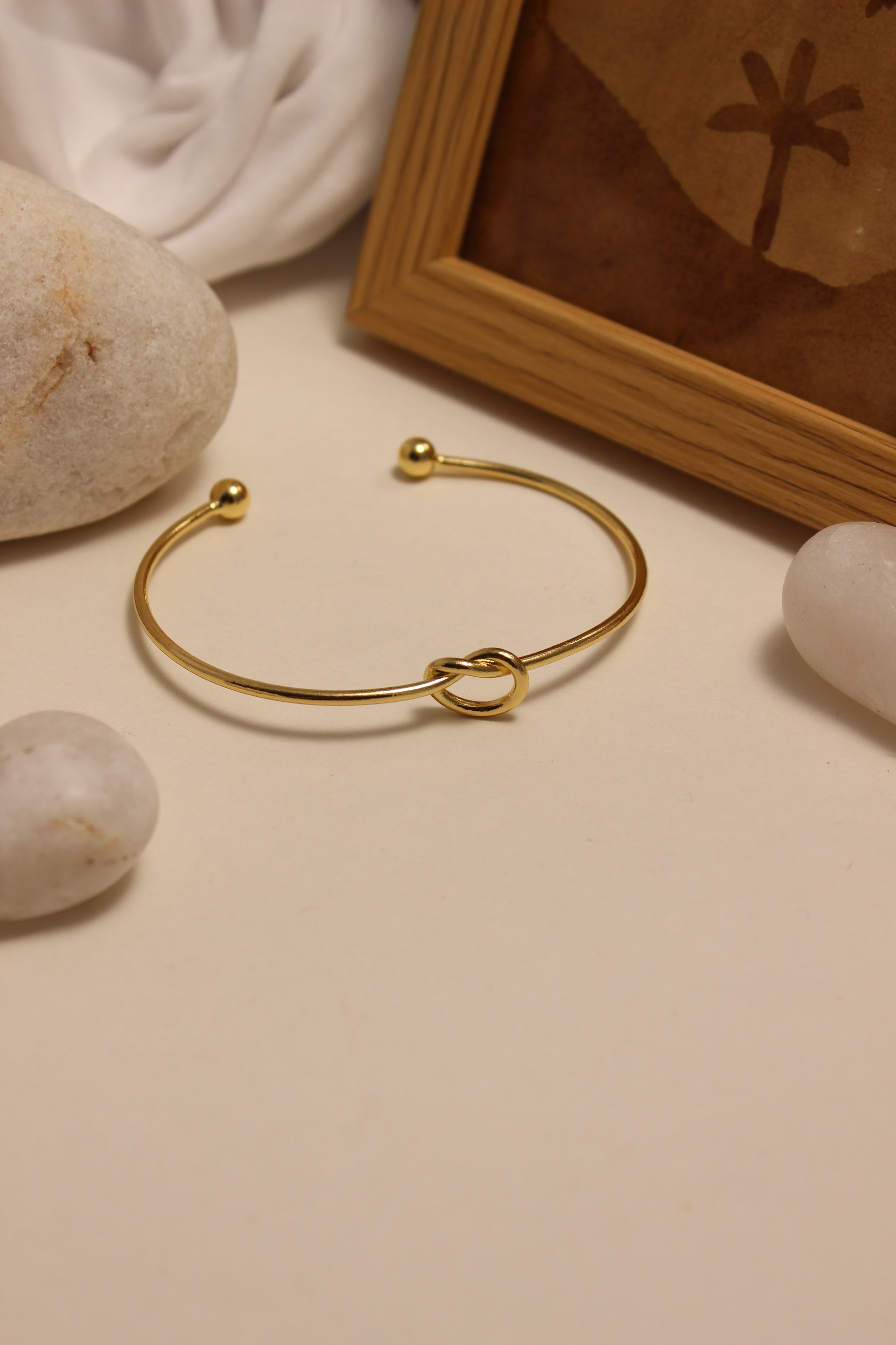 Entwine Cuff Bracelet on a beige surface with stones and a wooden box