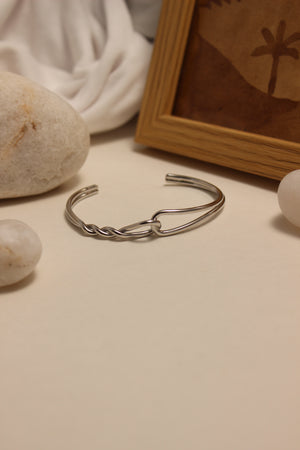 Sterling Dualis Cuff Bracelet on a textured surface with stones and a wooden frame in the background