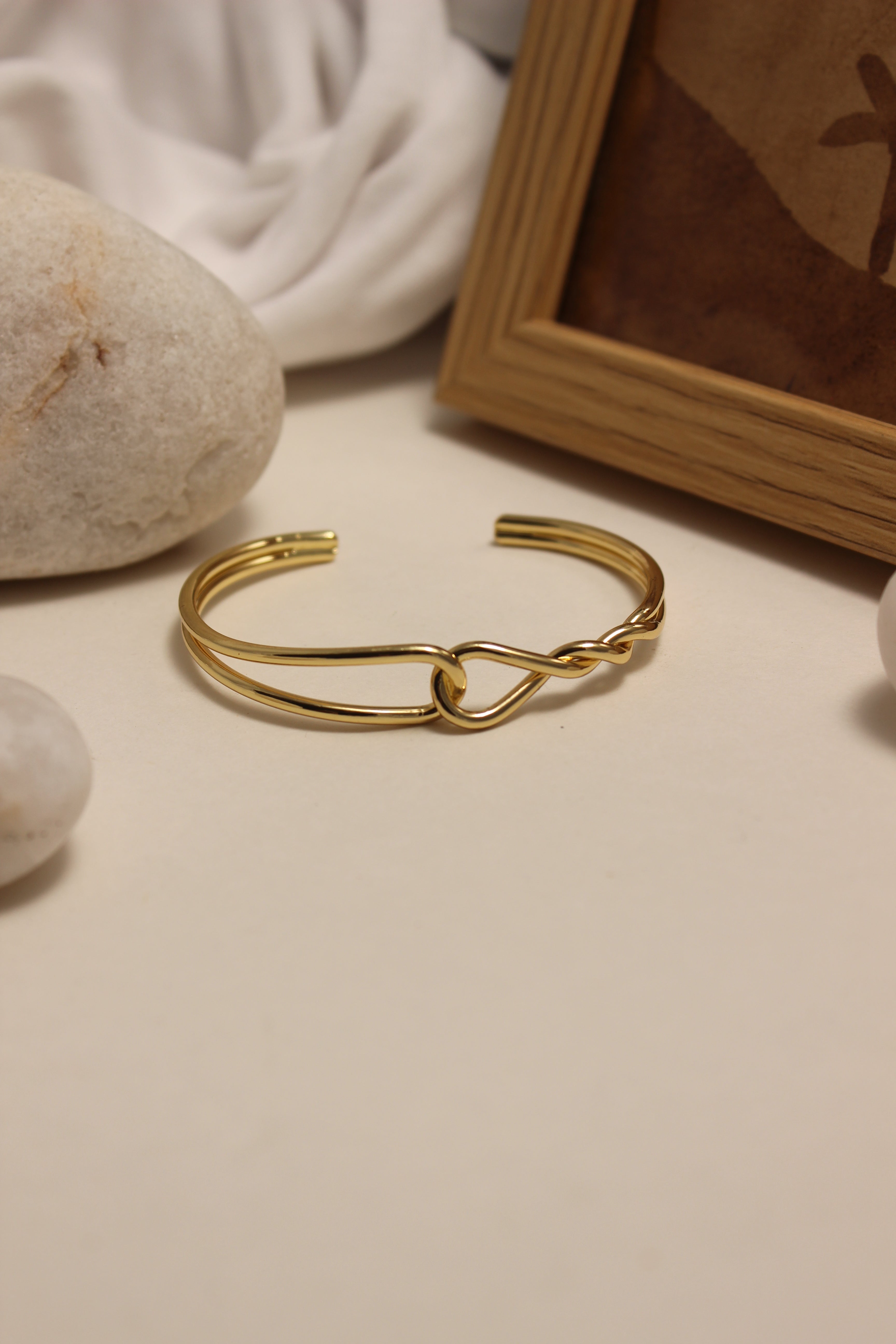 Aurum Dualis Cuff Bracelet on a neutral background with stones and fabric