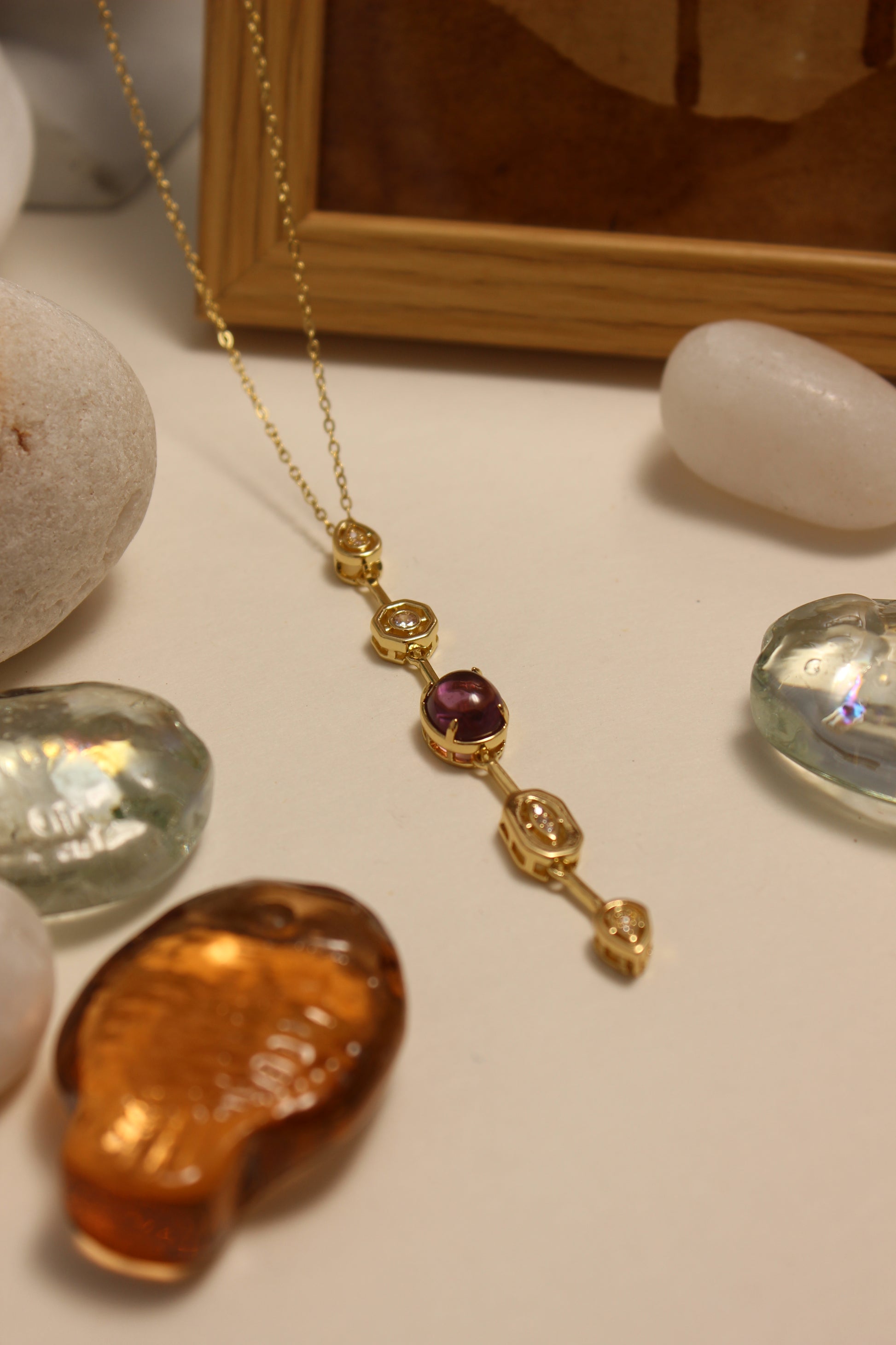 Viola Cascade Necklace on a surface with stones, seashells and wooden frame