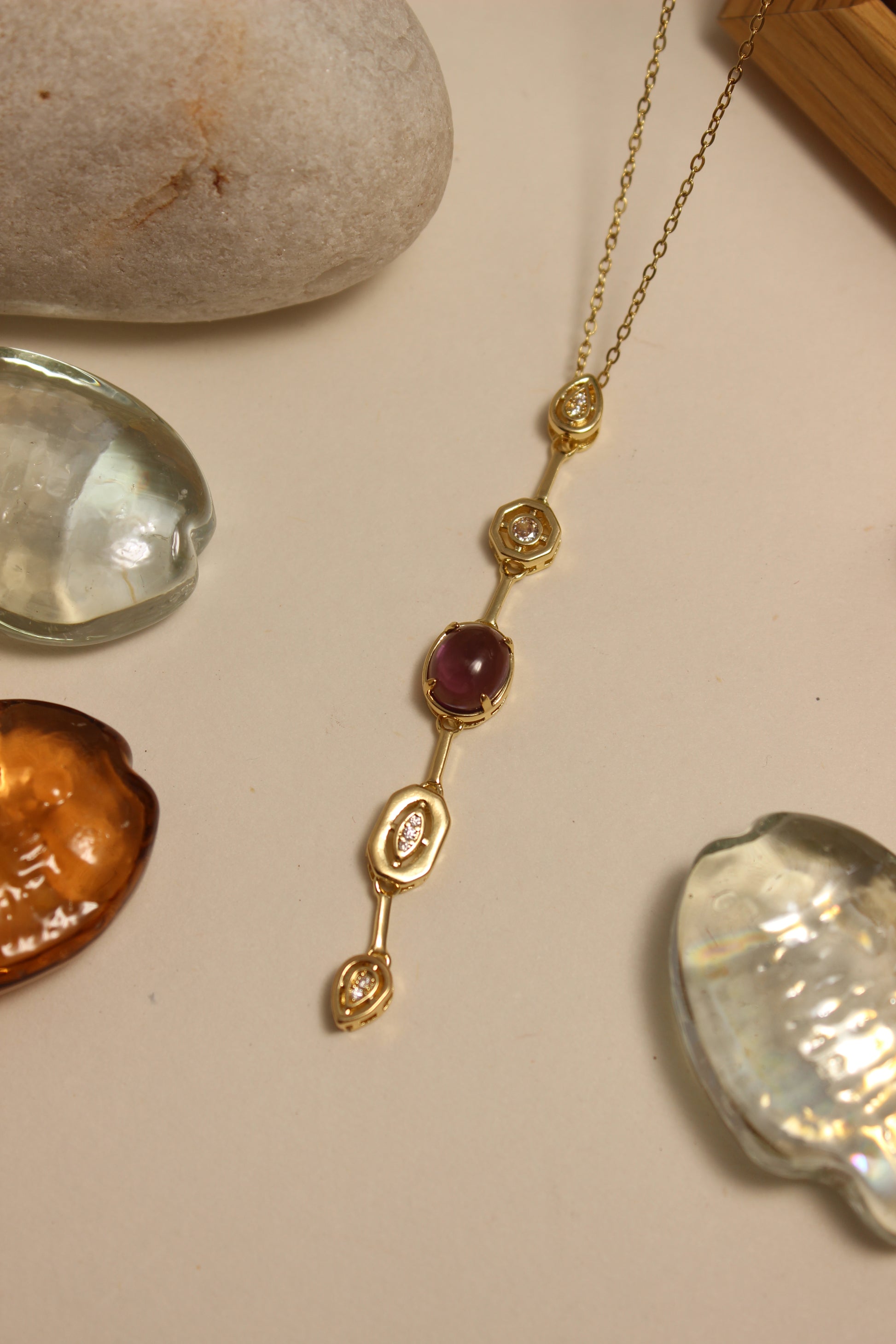 Viola Cascade Necklace on a beige surface with stones and seashells