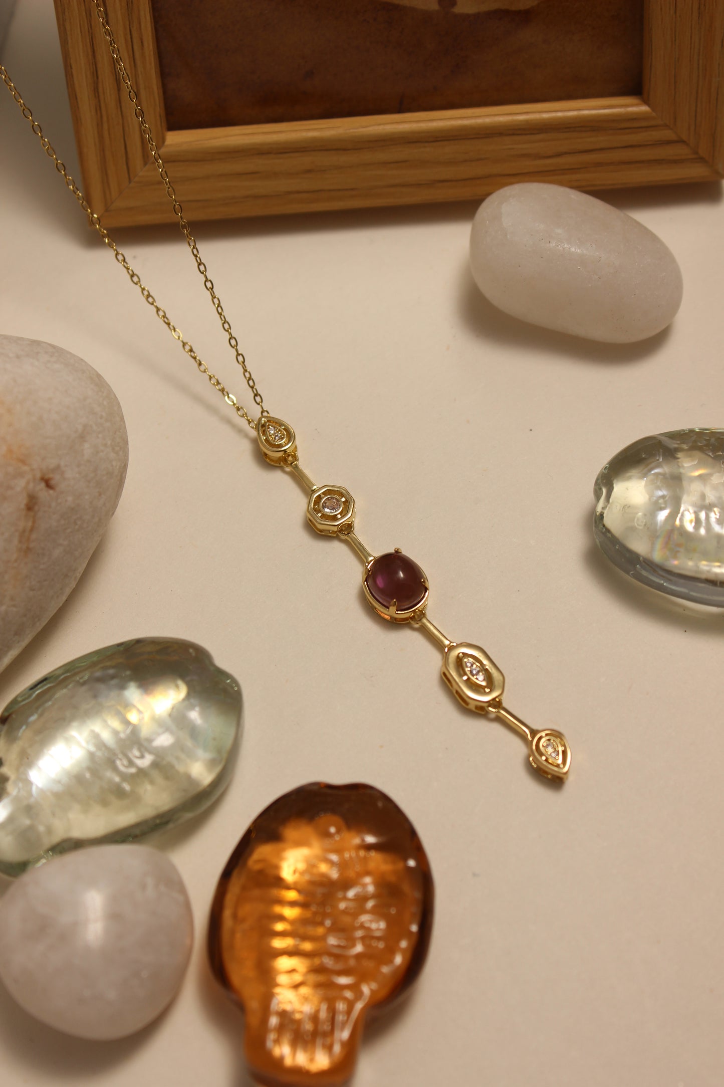 Viola Cascade Necklace on a surface with stones and a wooden frame