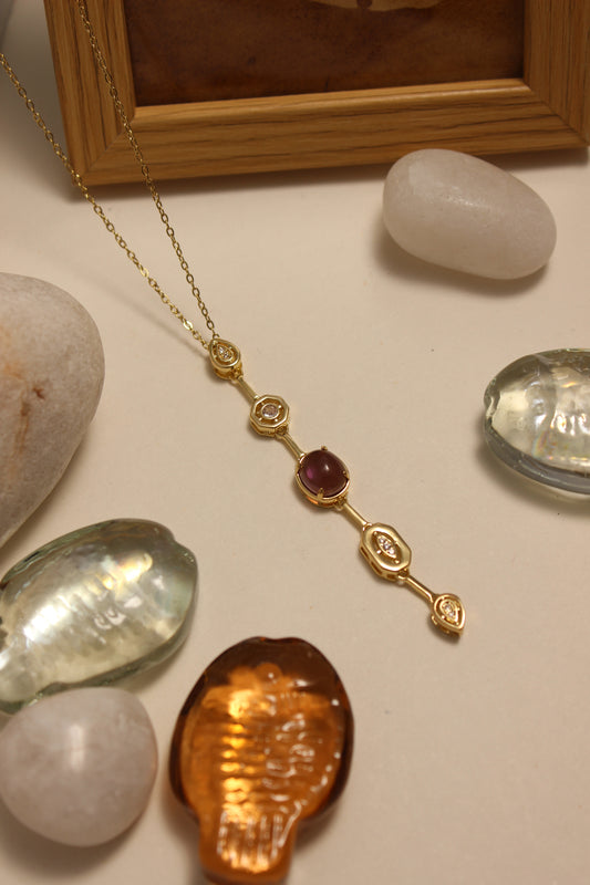 Viola Cascade Necklace on a surface with stones and a wooden frame