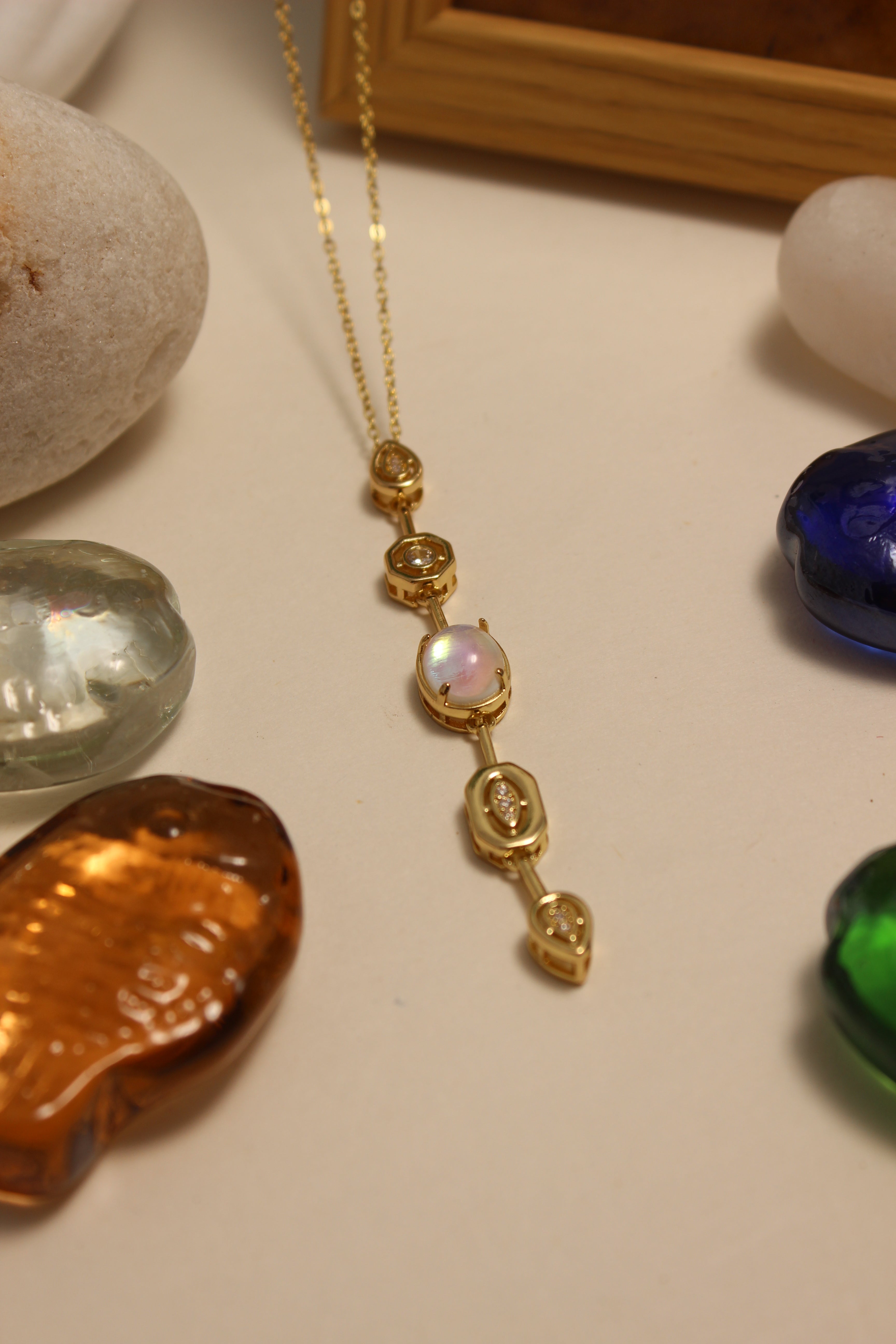 Seraphine Necklace on a surface with colorful stones and a framed picture