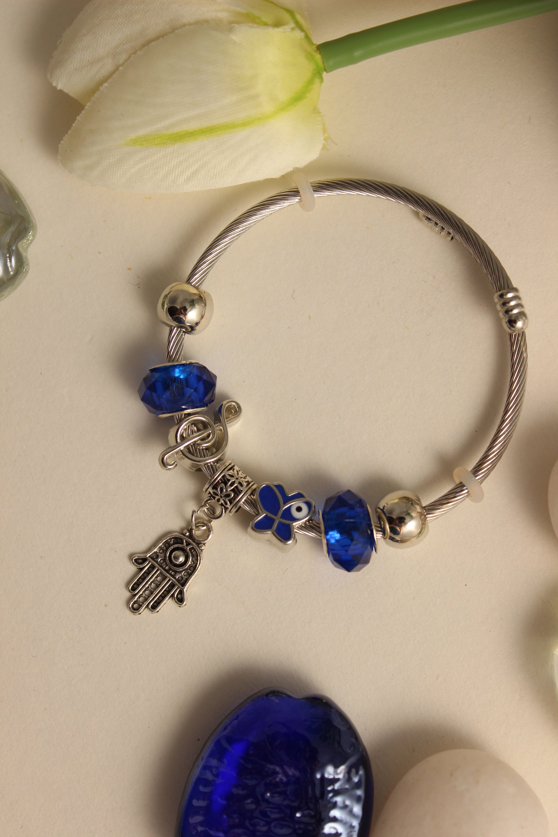 Mystic Iris Bracelet with blue beads and charms on a light surface with a flower and seashell