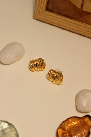 Elektra Stud Earrings on a light surface with stones and seashell
