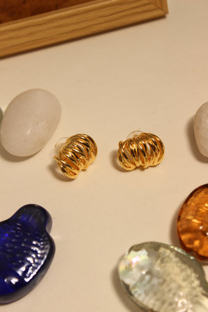 Elektra Stud Earrings on a textured surface with stones and seashell