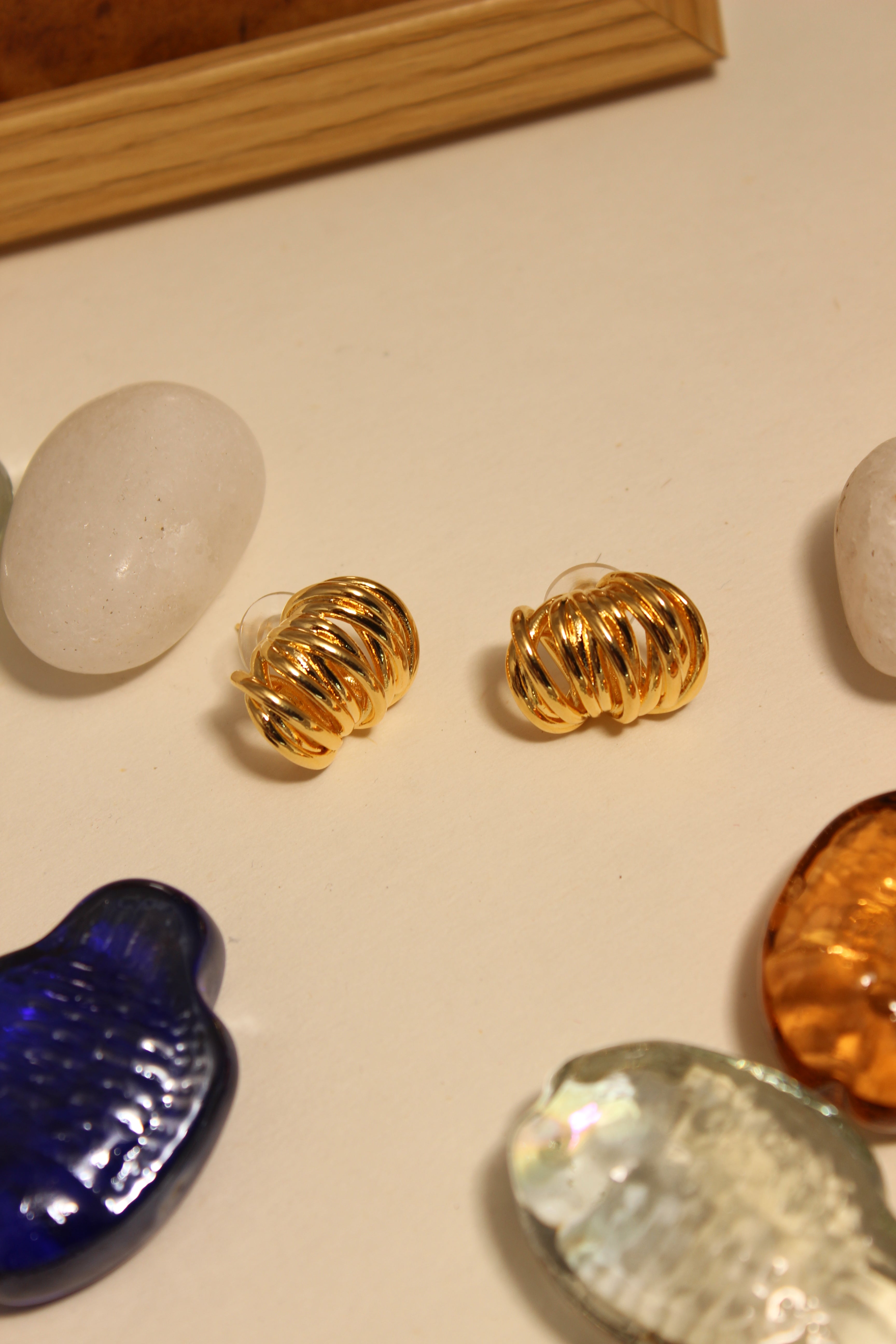 Elektra Stud Earrings on a textured surface with stones and seashell