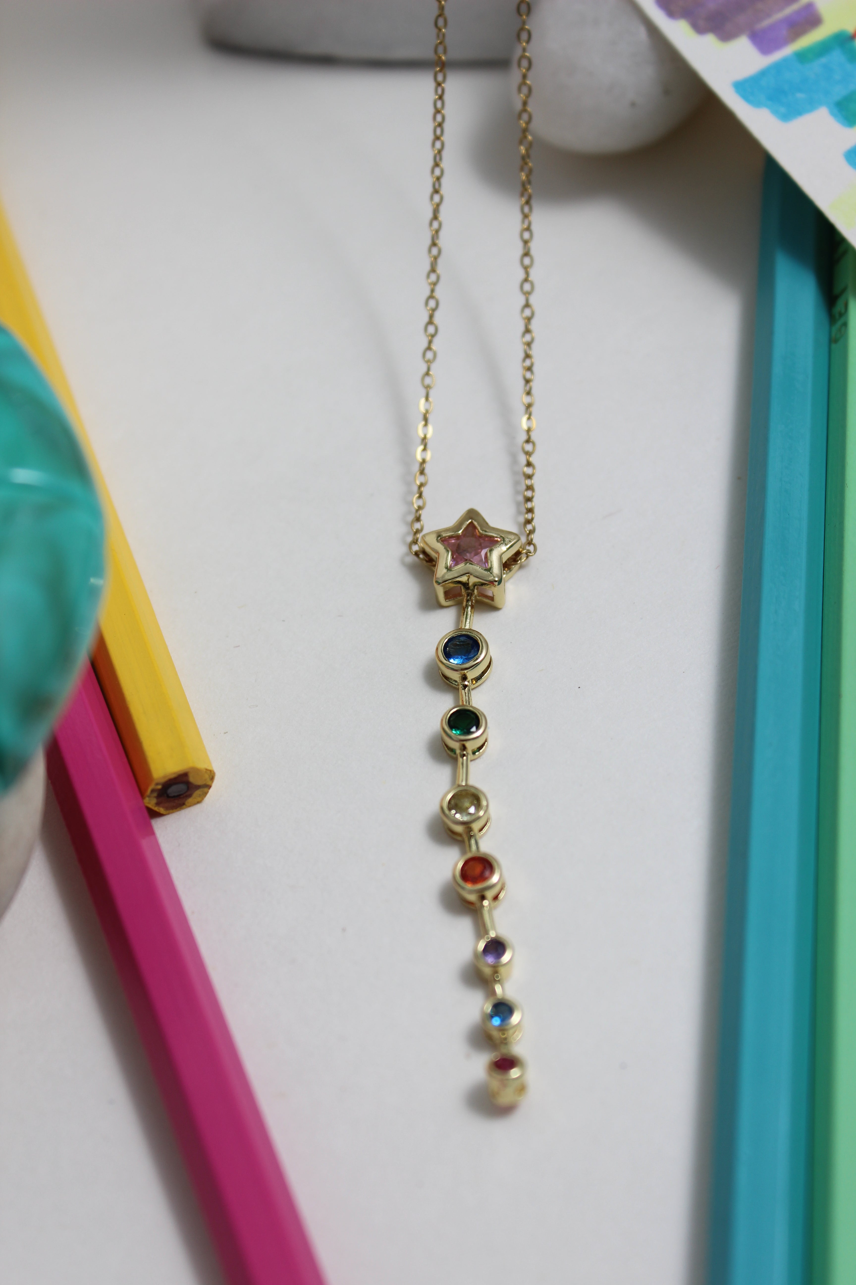 Nova Drip Necklace with colorful stones on a white surface with colorful objects around
