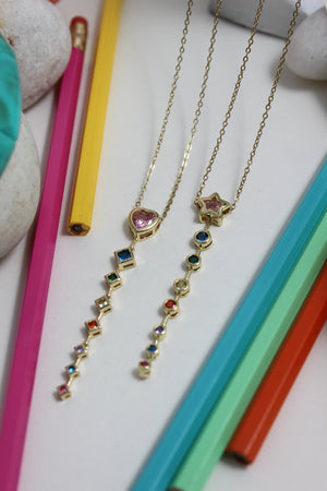 Rose Descent Necklace on a white surface with colorful pencils