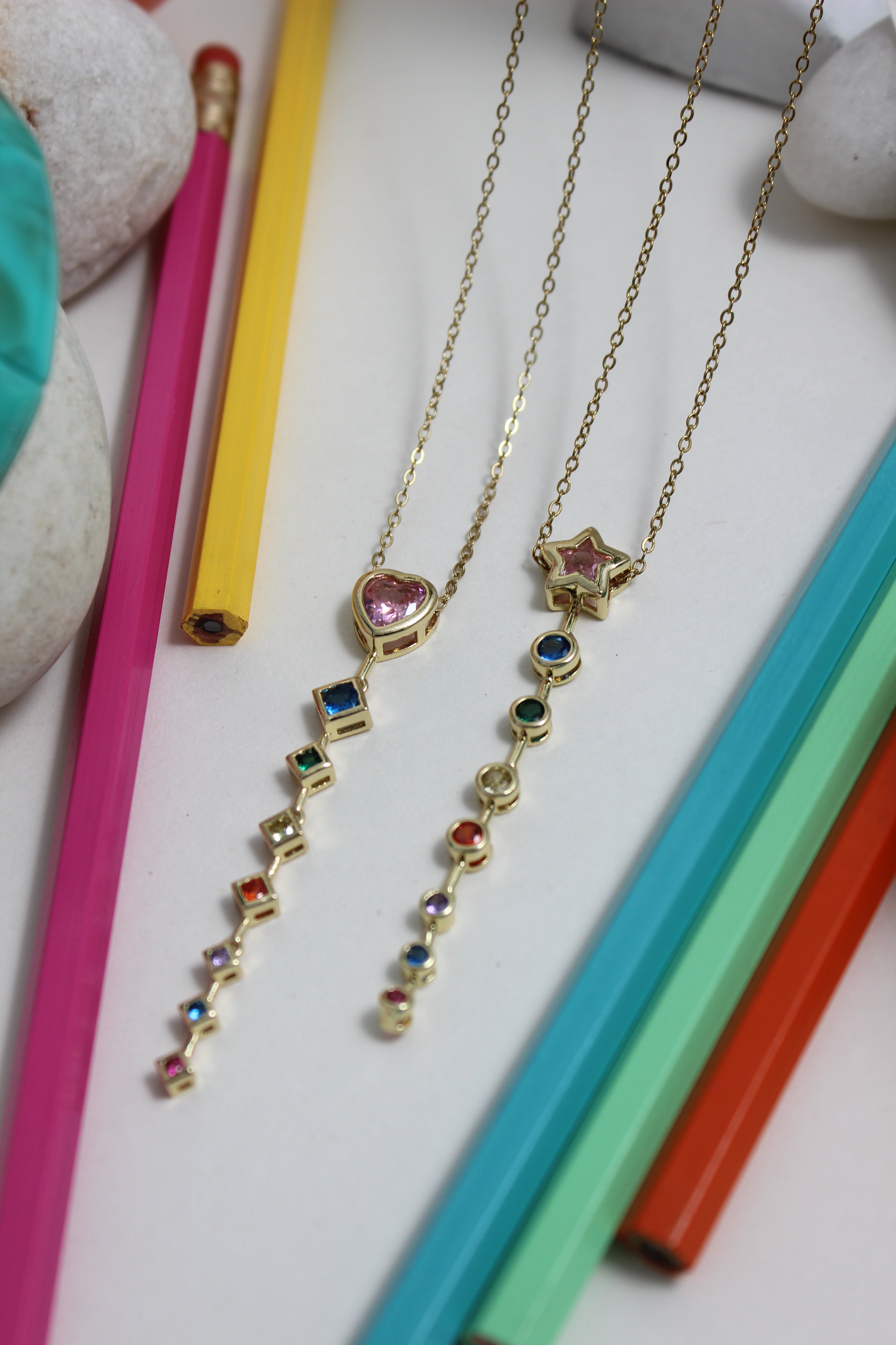 Rose Descent Necklace on a white surface with colorful pencils