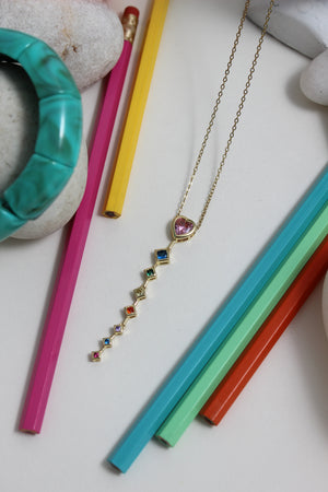 Rose Descent Necklace with colorful gemstones on a white surface with pencils