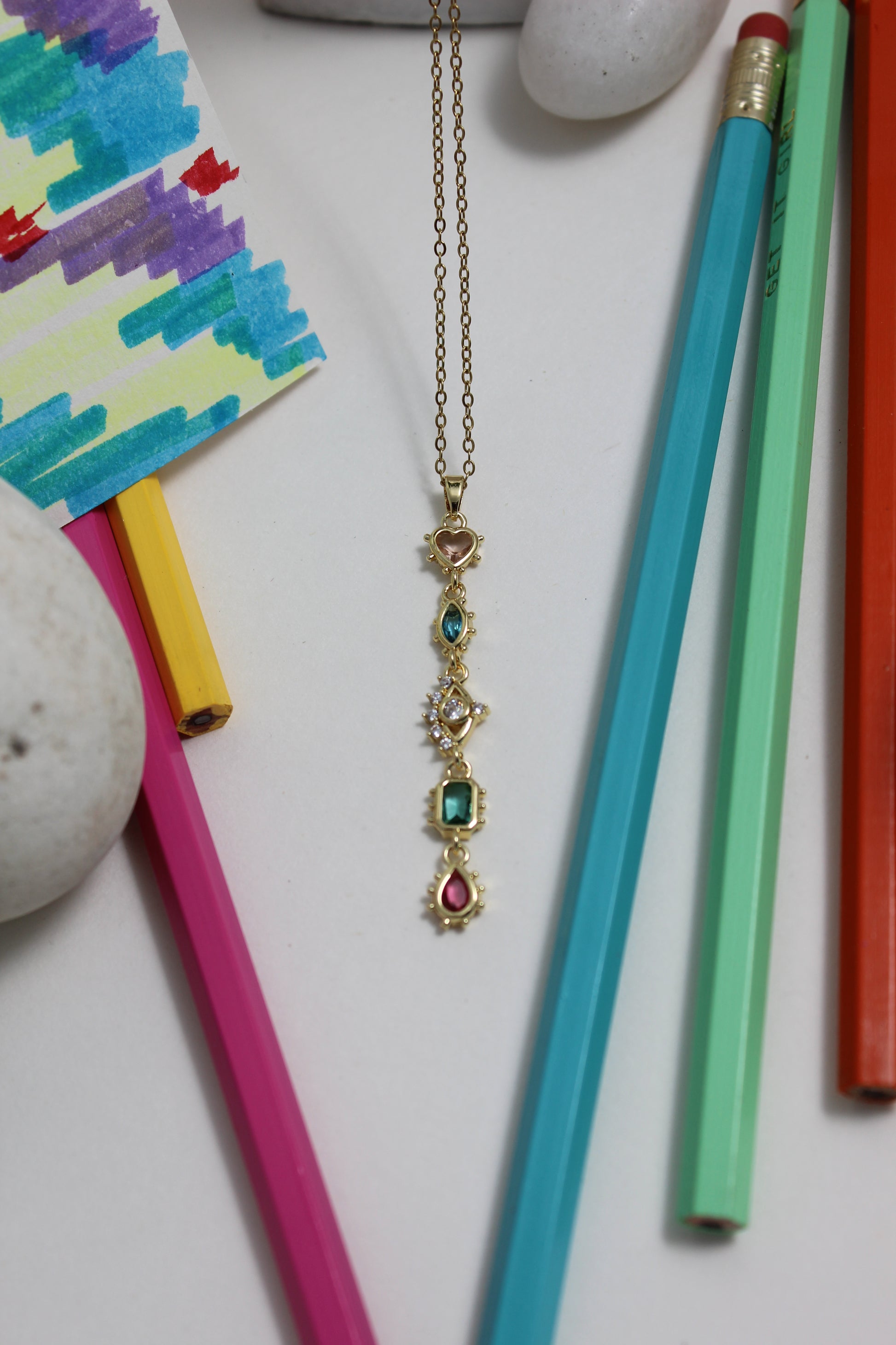 Colorful pencils and a decorative Fortuna Necklace on a white surface