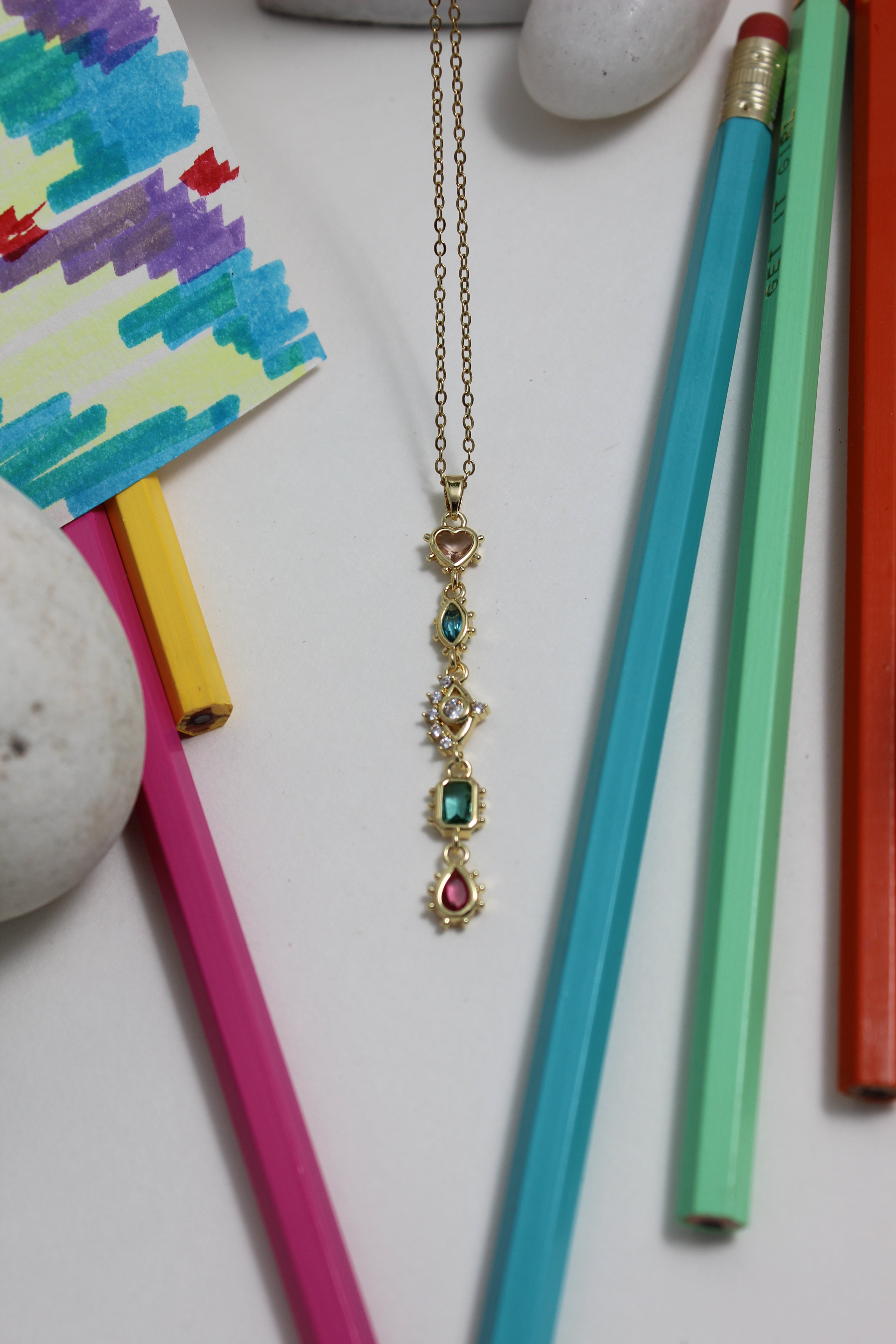 Colorful pencils and a decorative Fortuna Necklace on a white surface