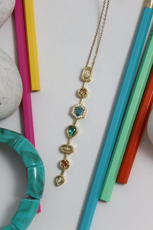 Stellar Pour Necklace with gemstones on a white surface with colorful pencils and a turquoise bracelet