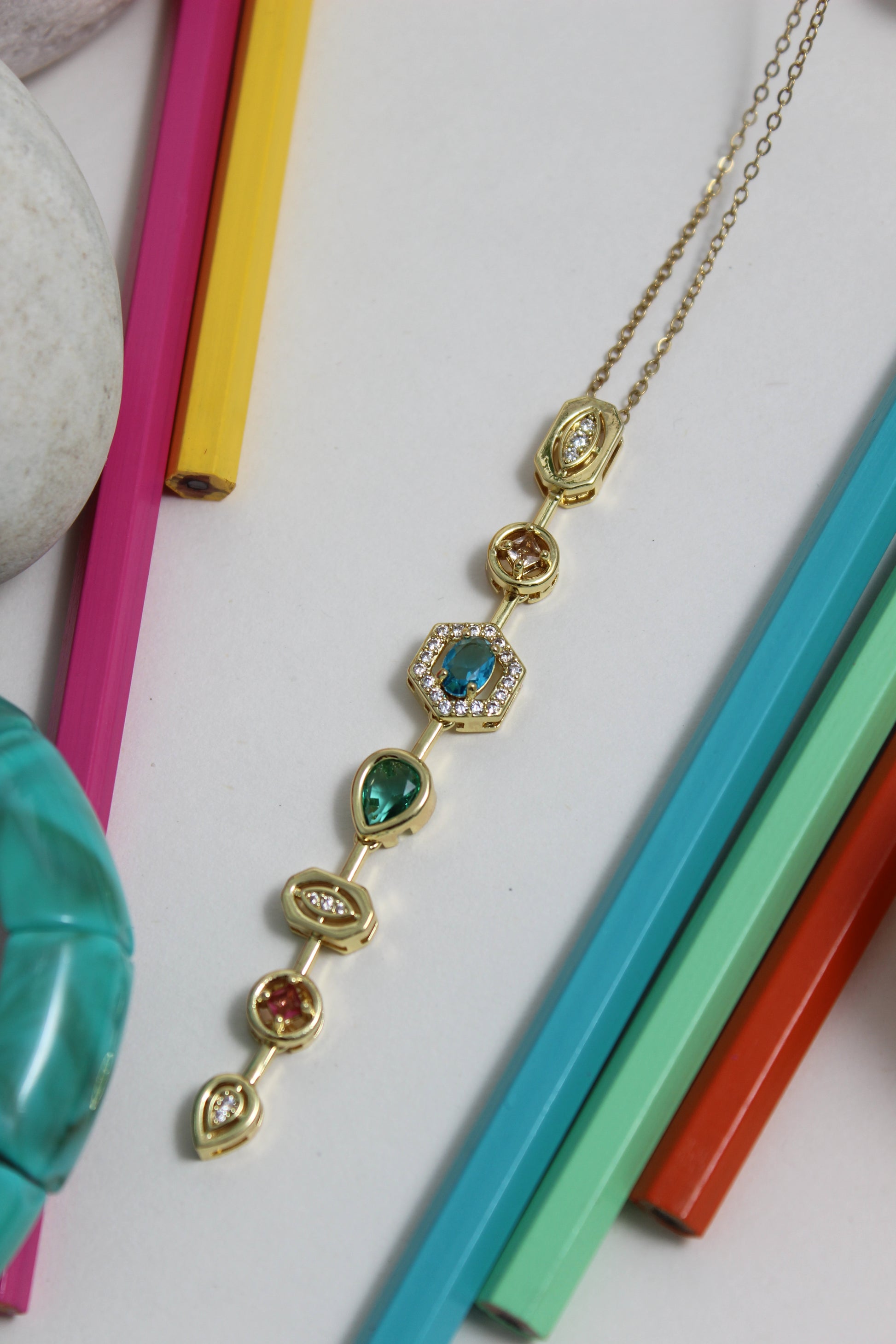 Stellar Pour Necklace with colorful gemstones on a white surface with colorful pencils