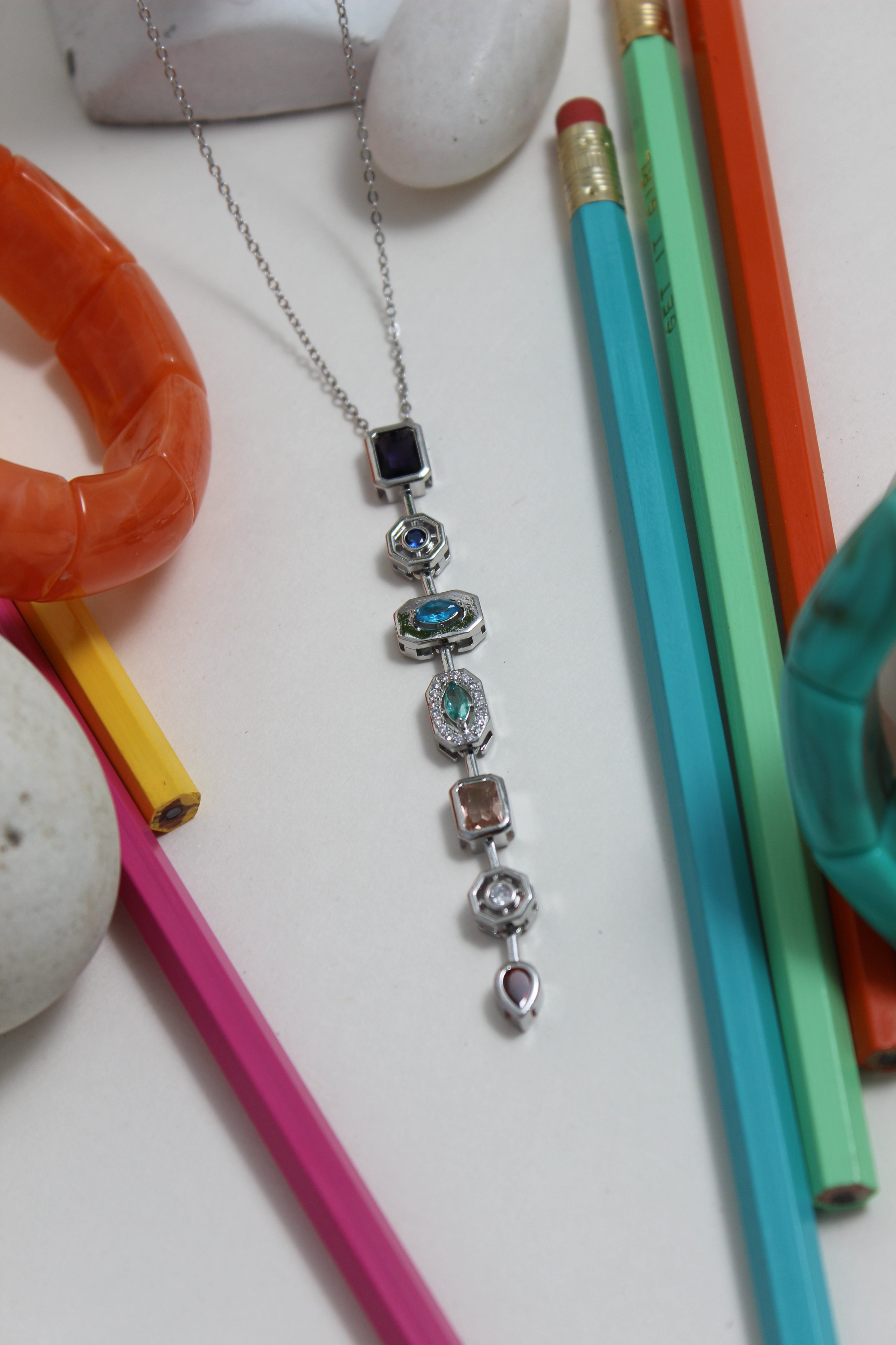 Argent Pastel Pour Necklace with colorful beads on a white surface with colorful pencils