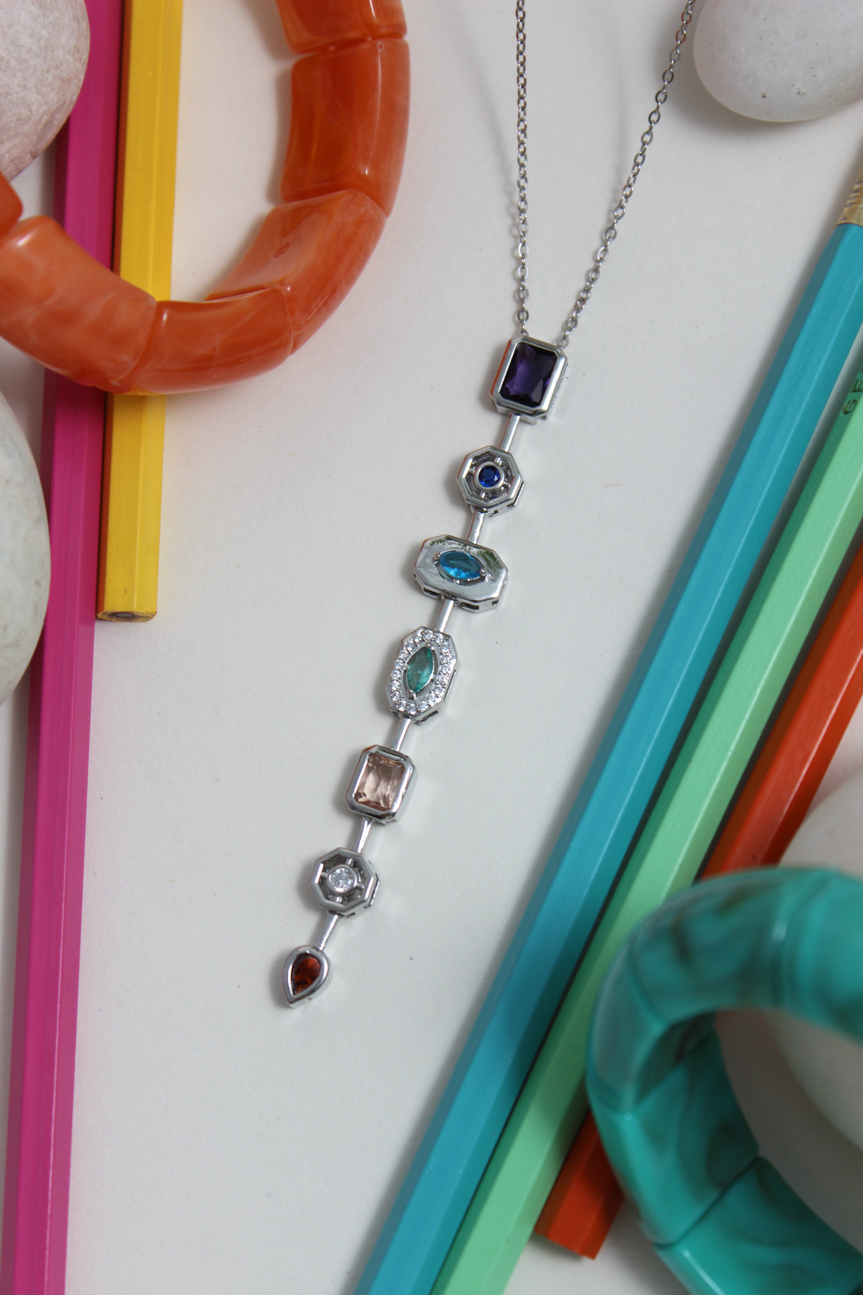 Argent Pastel Pour Necklace with colorful gemstones on a white surface with colorful pencils and stones