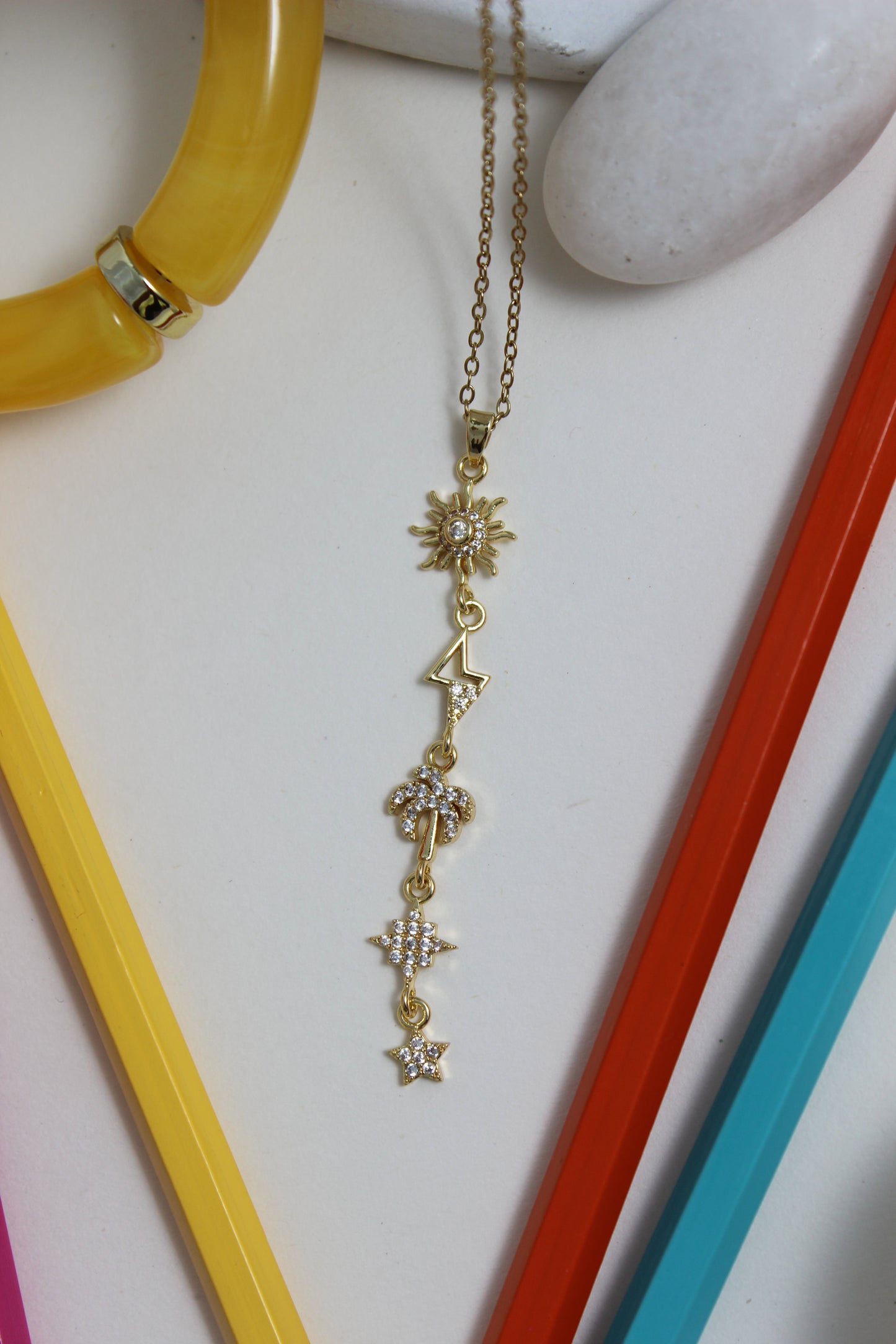 Golden Palm Necklace with star designs on a white surface with colorful pencils and stone