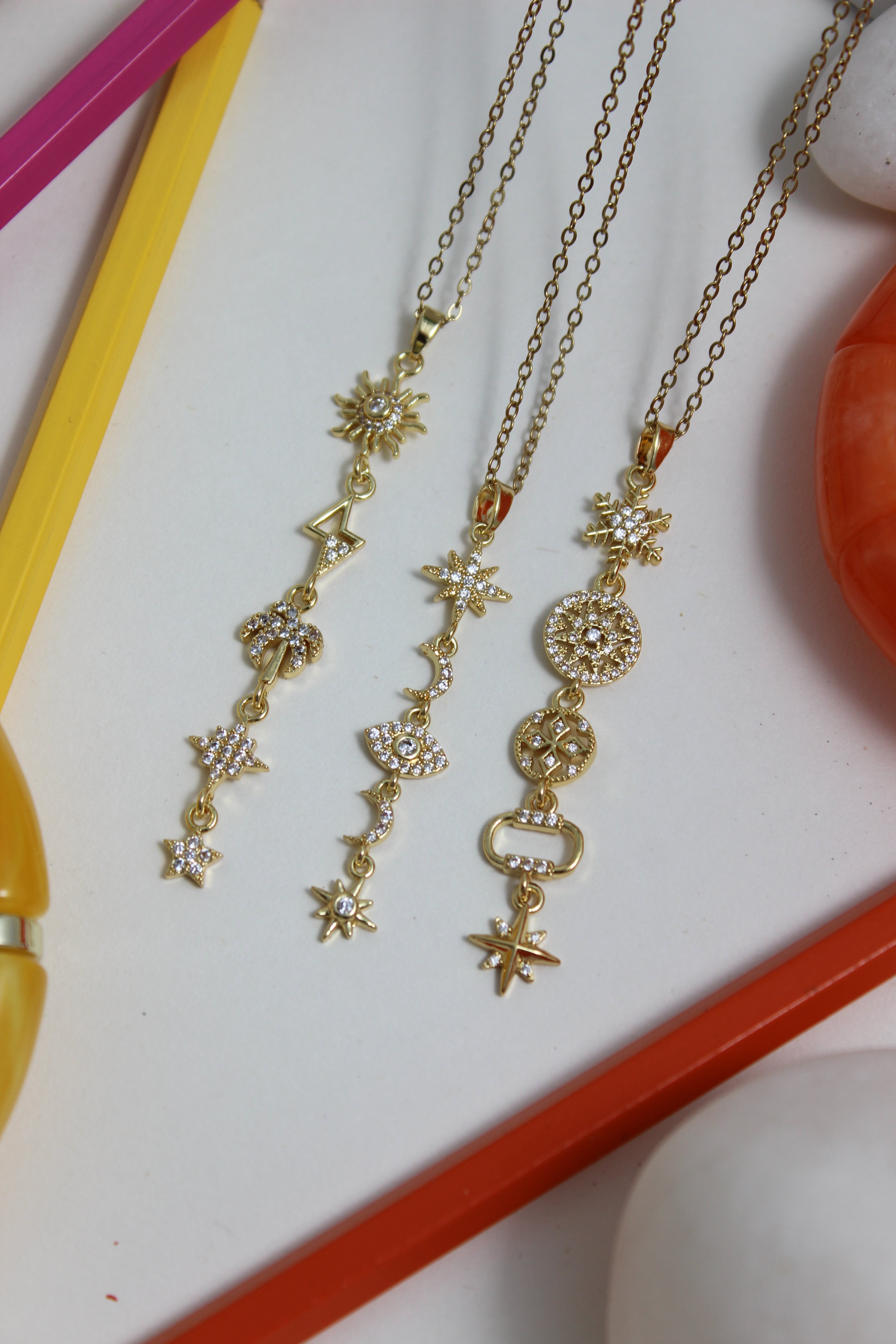 Northbloom Necklace with star-shaped pendants on a white surface with a colorful pencils