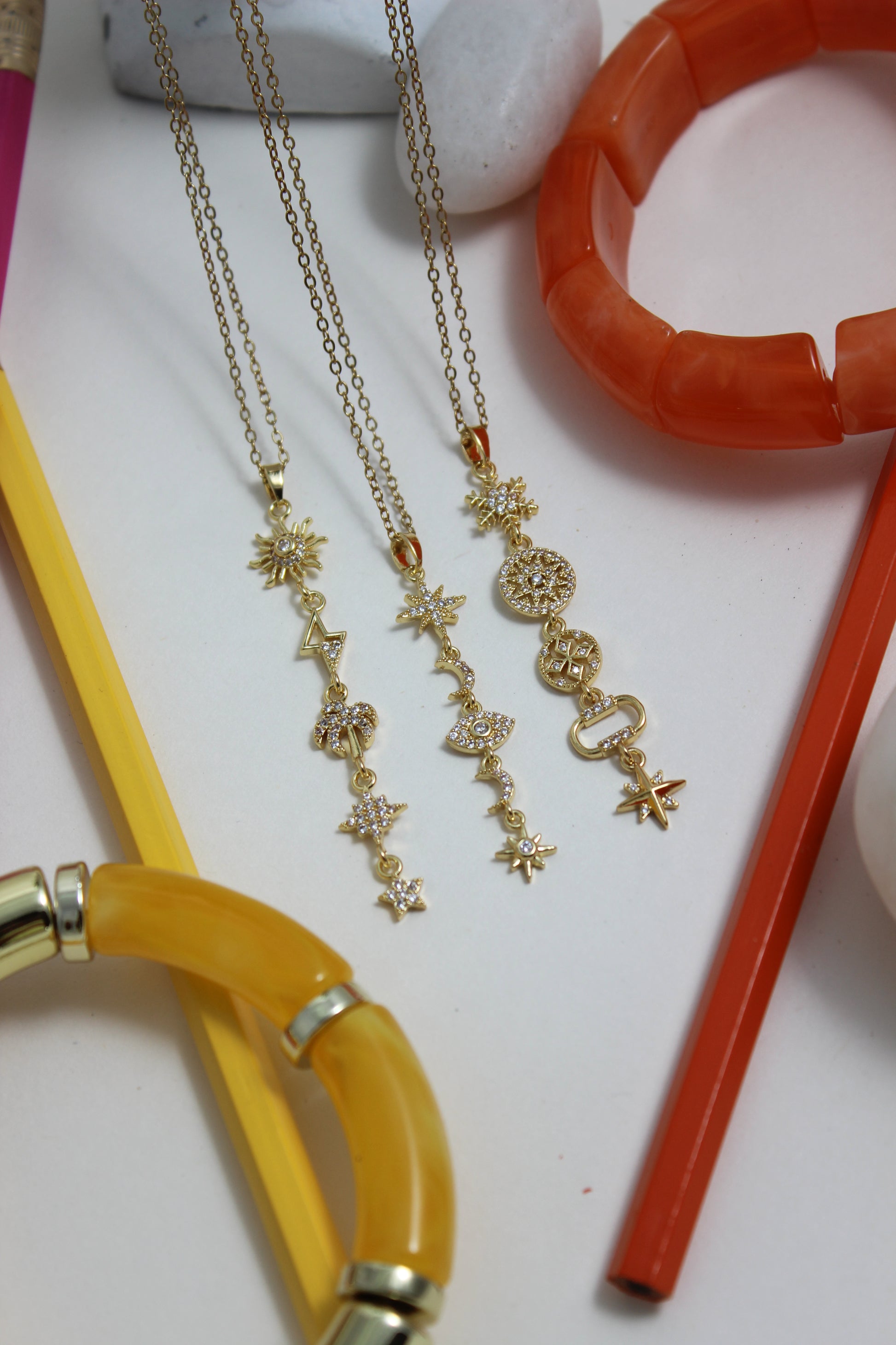 Golden Palm Necklace with orange and yellow pencils on a white surface