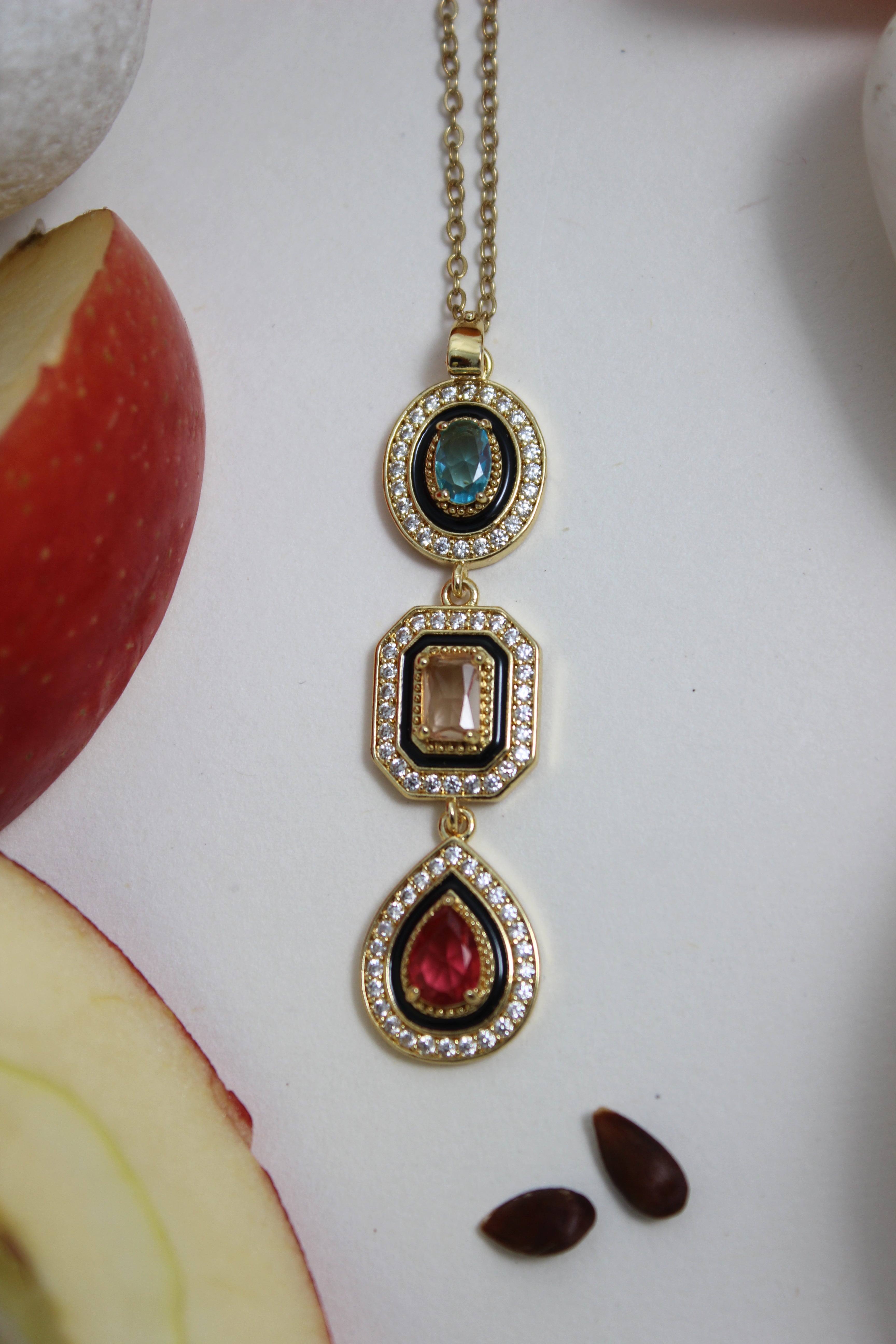Noir Royale Necklace with gemstones on a white surface with apples and seeds