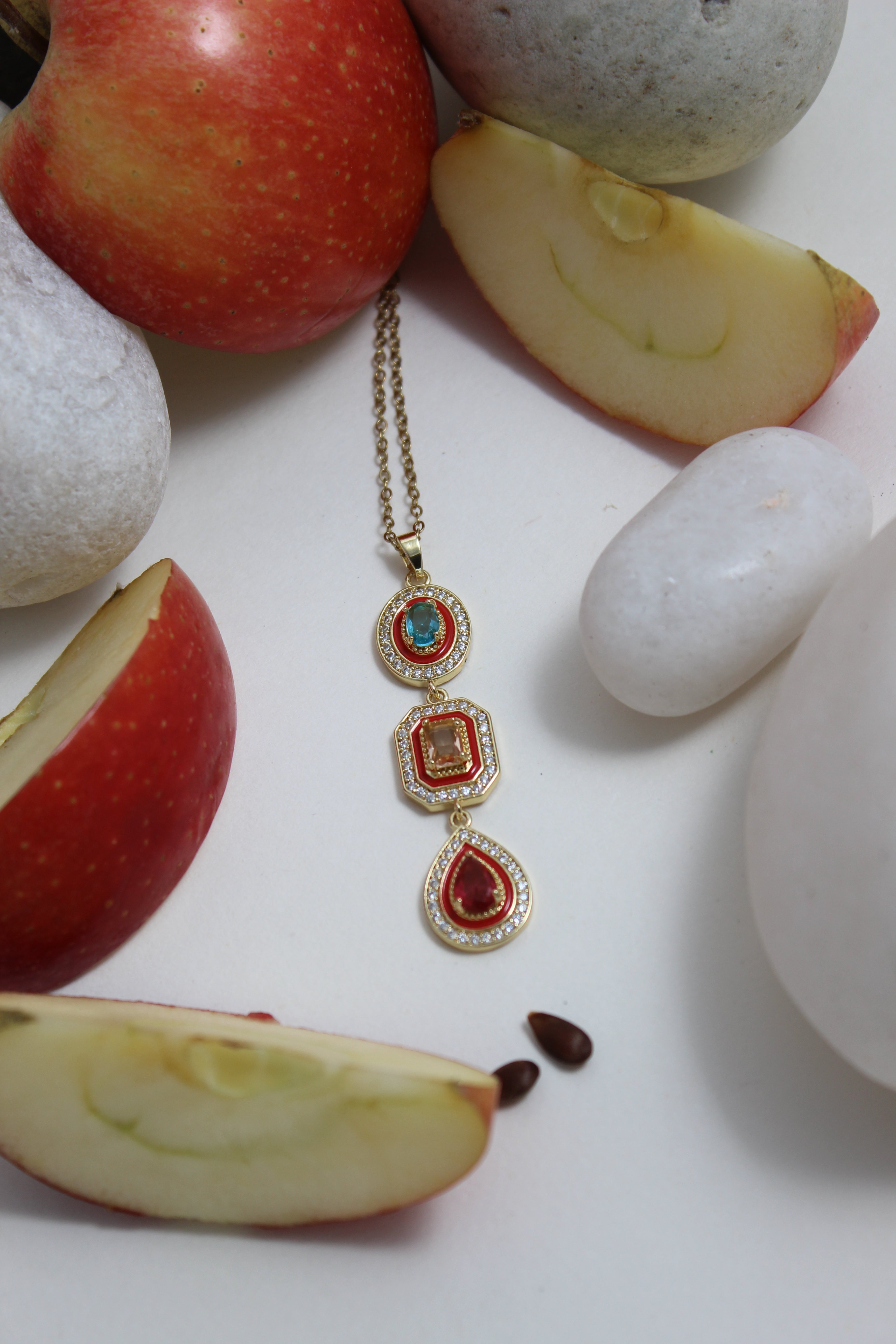 Empress Flame Necklace with red and blue stones on a white surface with apples and stones