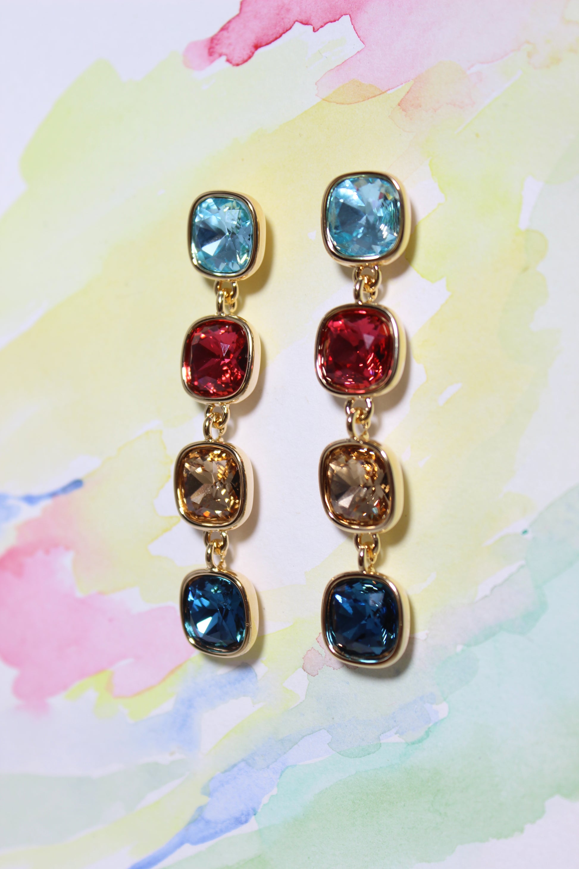 Radiant Skies Earrings with multicolored gemstones on a watercolor background