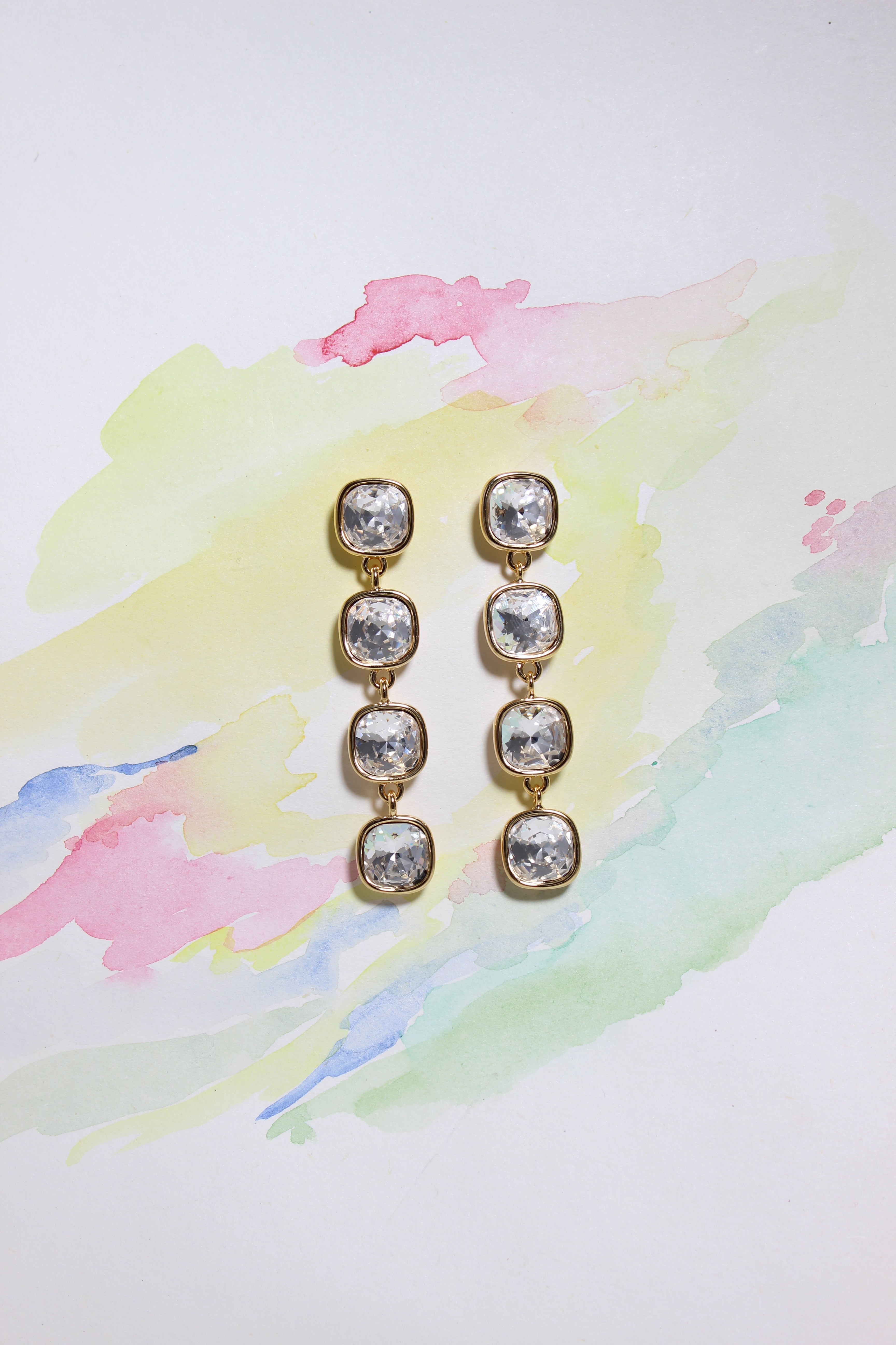Pair of Glacier Glow Earrings with clear stones on a colorful watercolor background