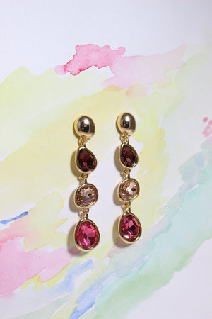 Gold Sienna Bloom Earrings with red and brown gemstones on a colorful watercolor background