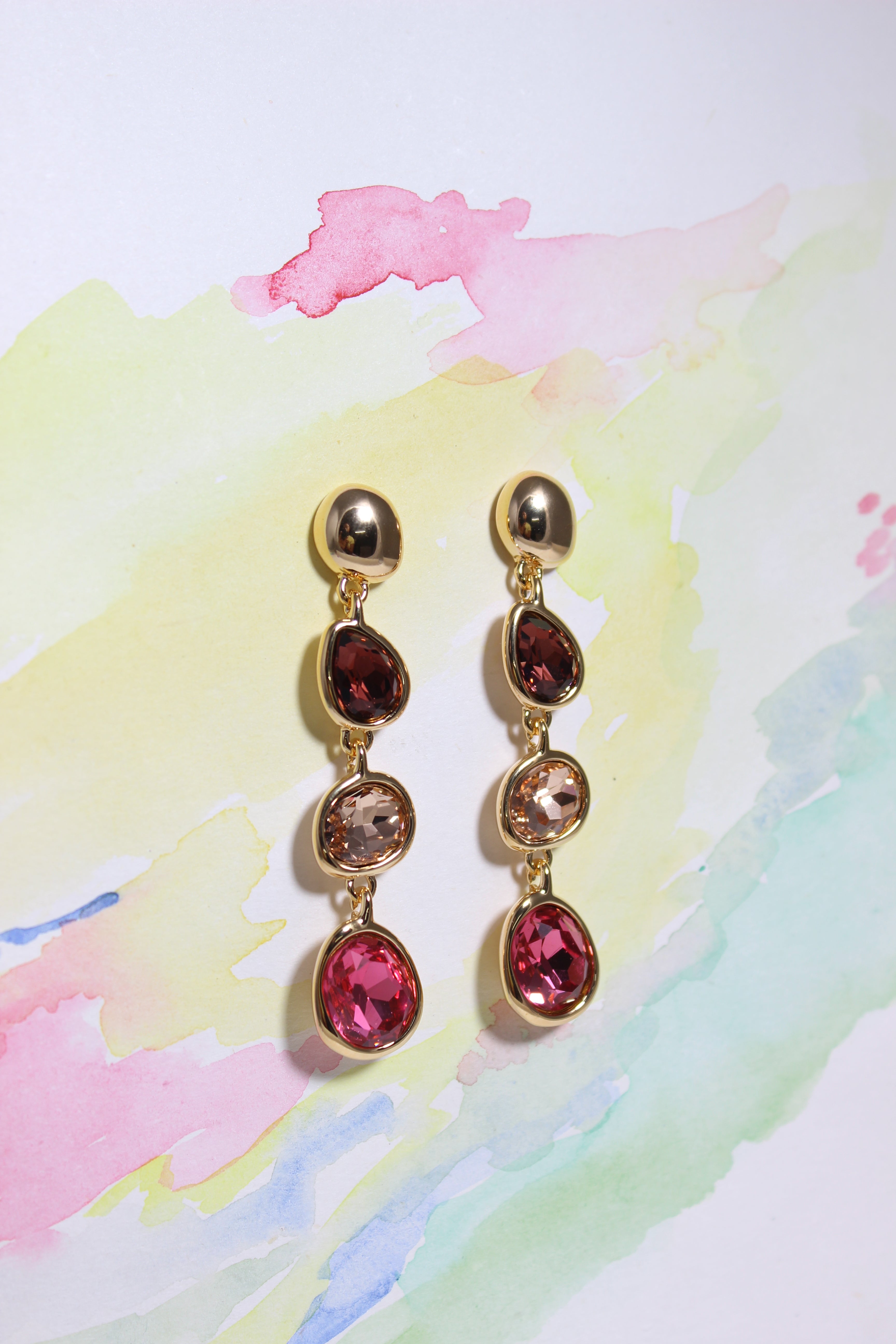 Gold Sienna Bloom Earrings with red and brown gemstones on a colorful watercolor background