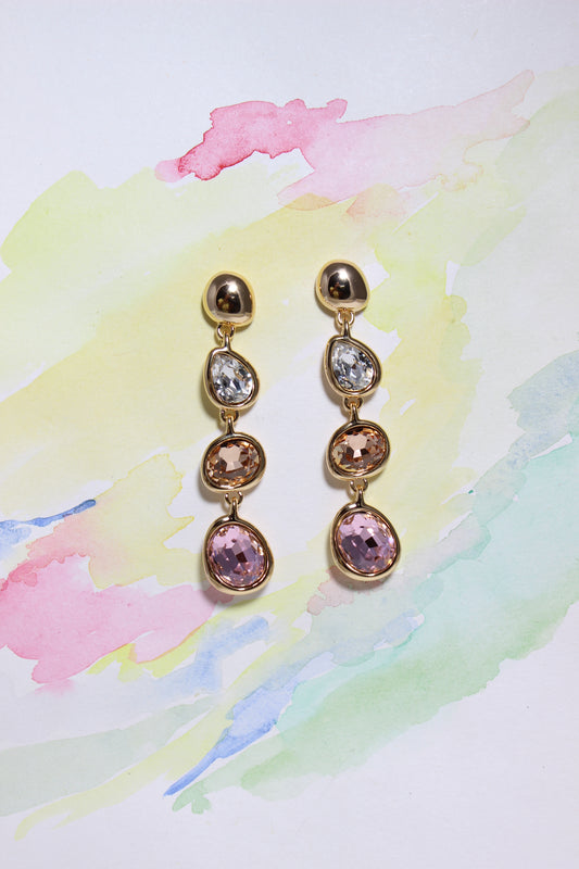 Pair of Auric Petals Earrings with pink and clear gemstones on a colorful watercolor background