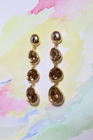 Gold Honeyfall Earrings with brown gemstones on a colorful watercolor background