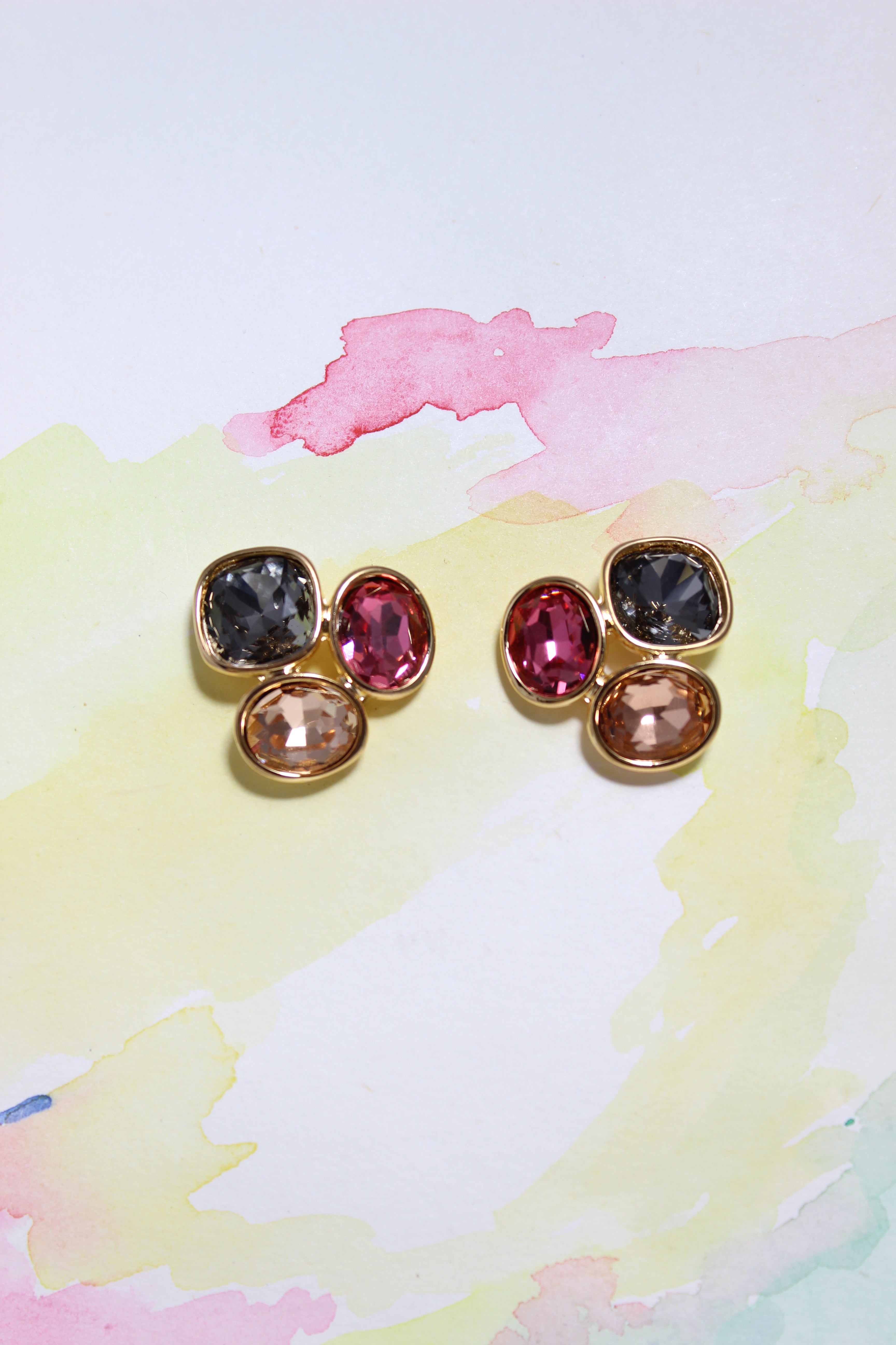 Pair of Solar Gleam Earrings with multicolored gemstones on a watercolor background