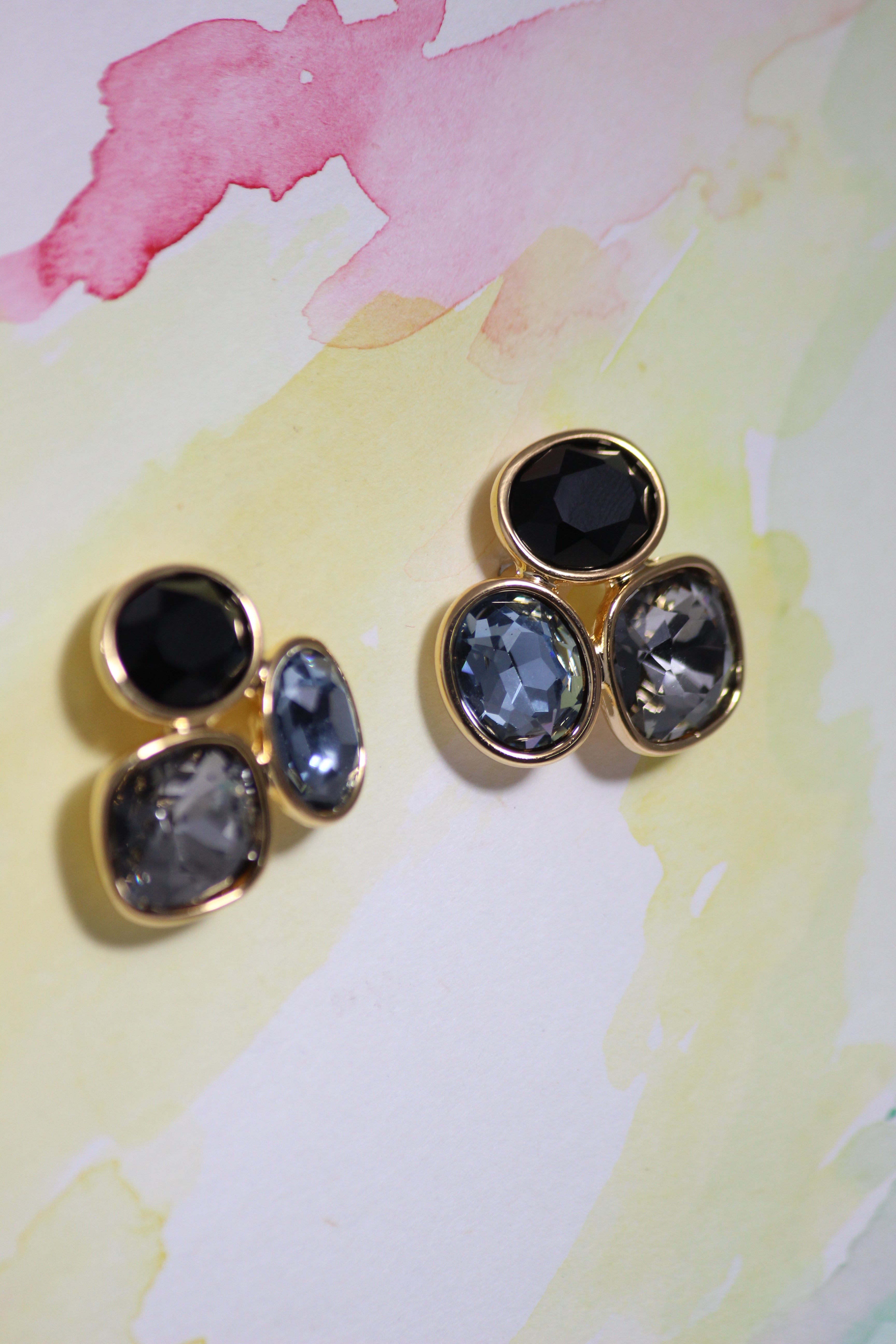 Pair of Blue Mirage Earrings with black and gold design on a watercolor background