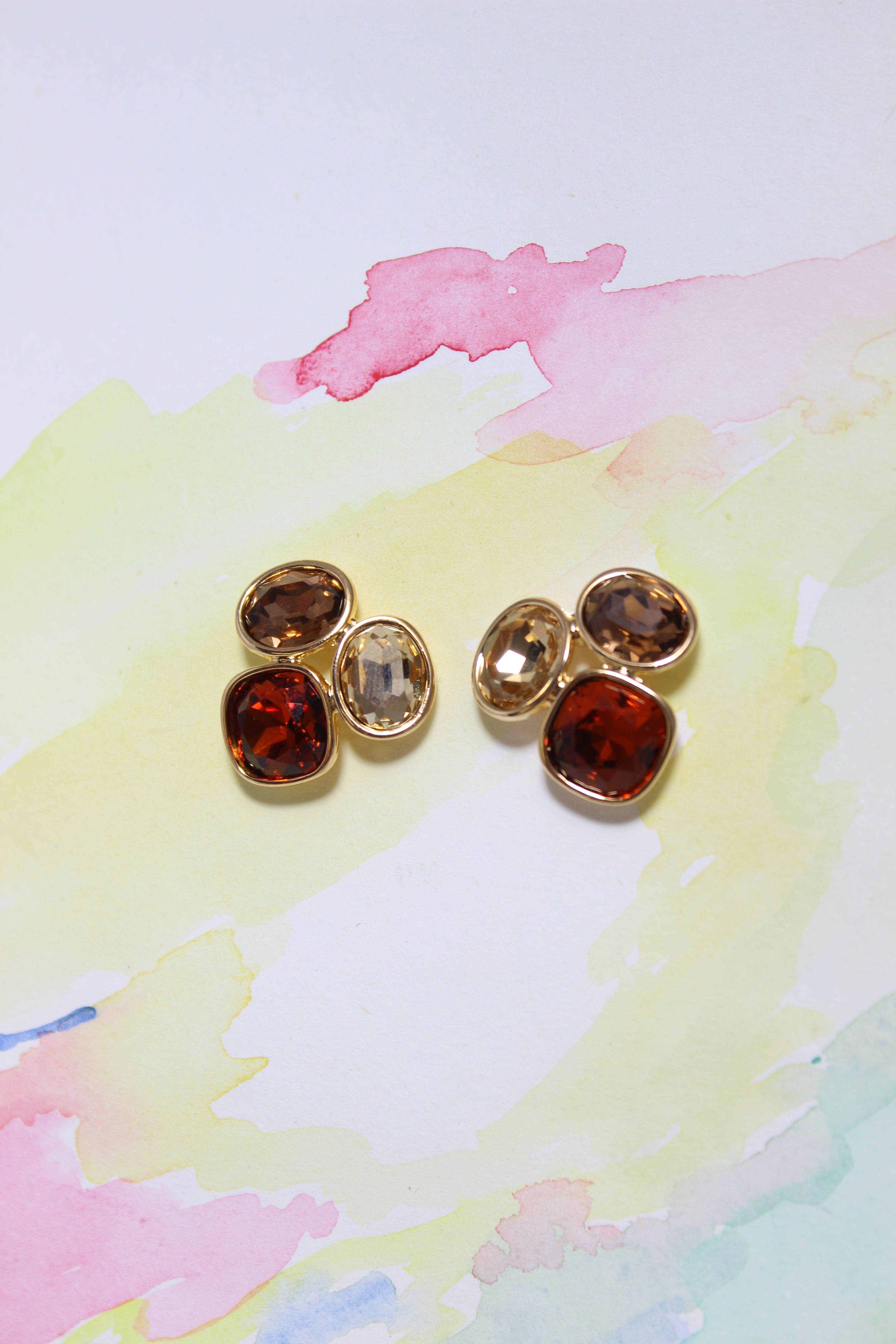 Pair of gold Sunflare Earrings with brown gemstones on a watercolor background