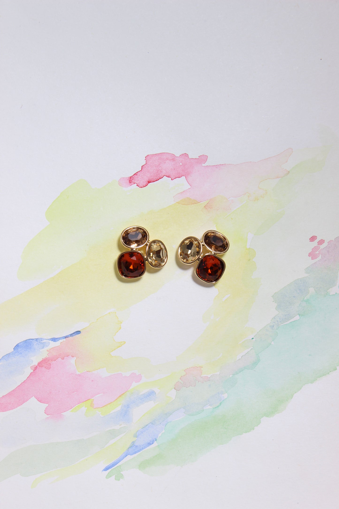 Gold Sunflare Earrings with red gemstones on a watercolor background