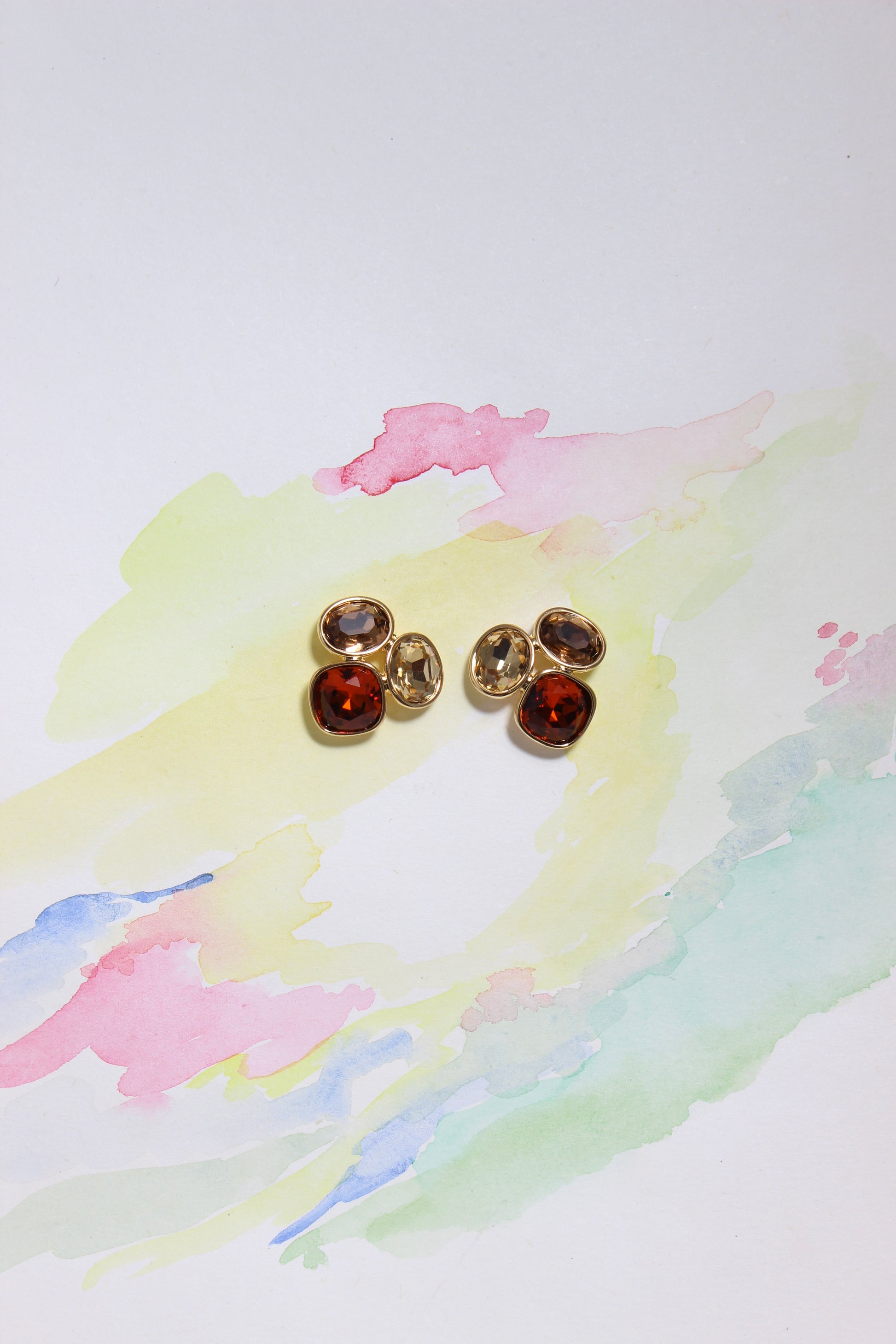 Gold Sunflare Earrings with red gemstones on a watercolor background
