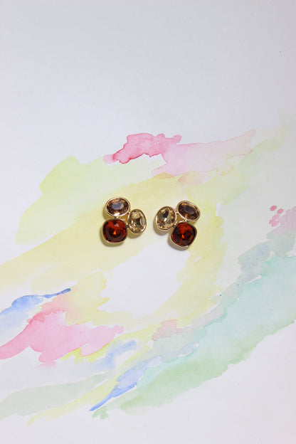 Gold Sunflare Earrings with red gemstones on a watercolor background
