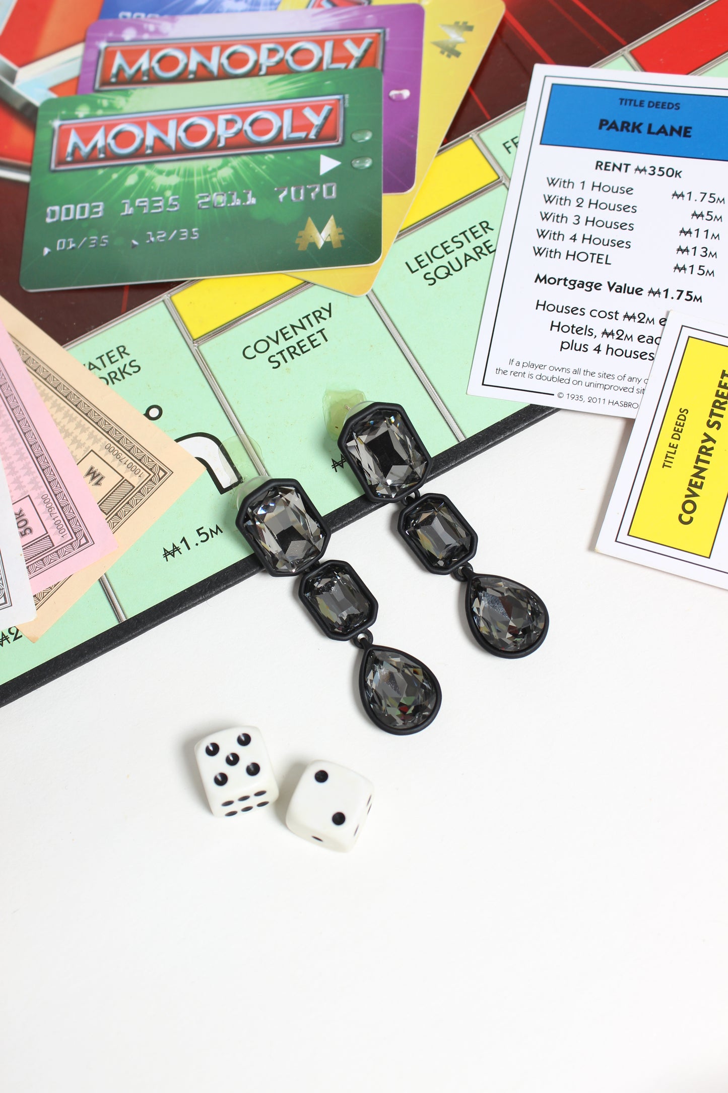 Monopoly game pieces and cards on a white background with Noir Flame Earrings