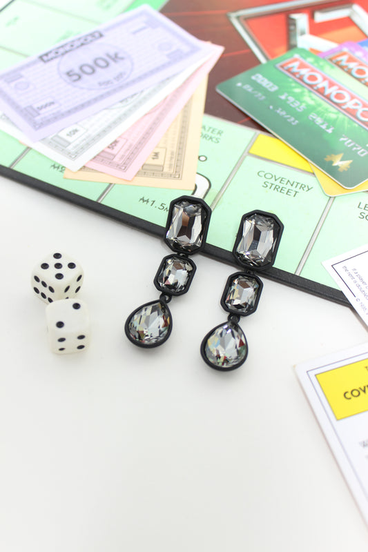 Noir Flame Earrings on a Monopoly board game with money and dice