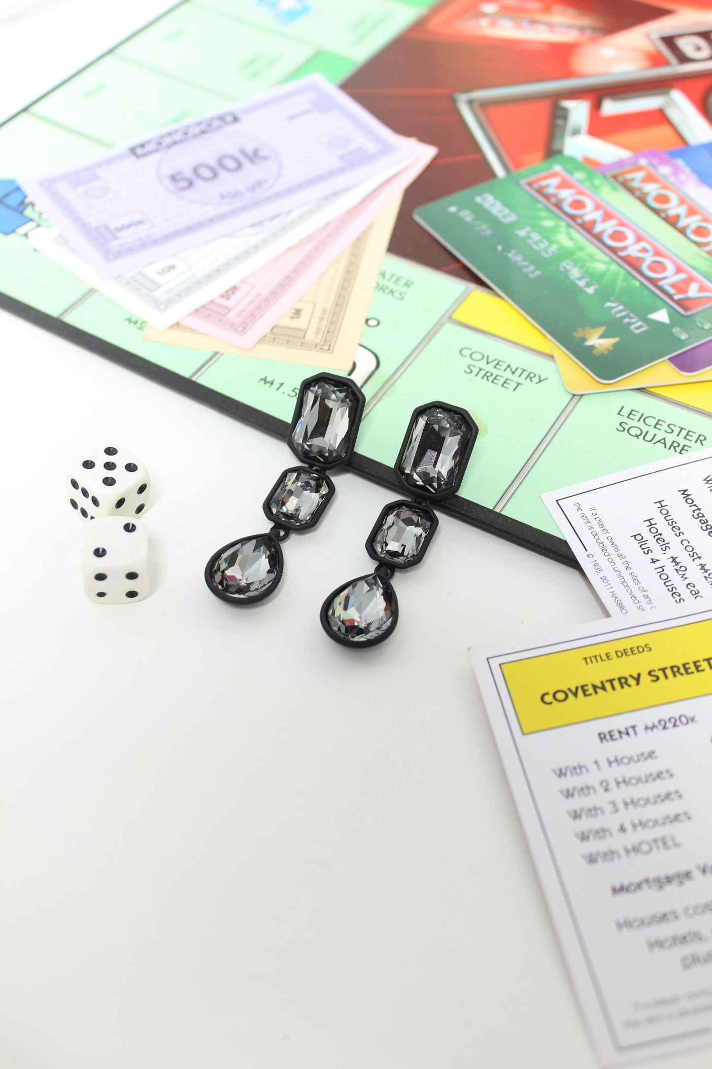 Close-up of a Monopoly game board with property cards and dice with Noir Flame Earrings